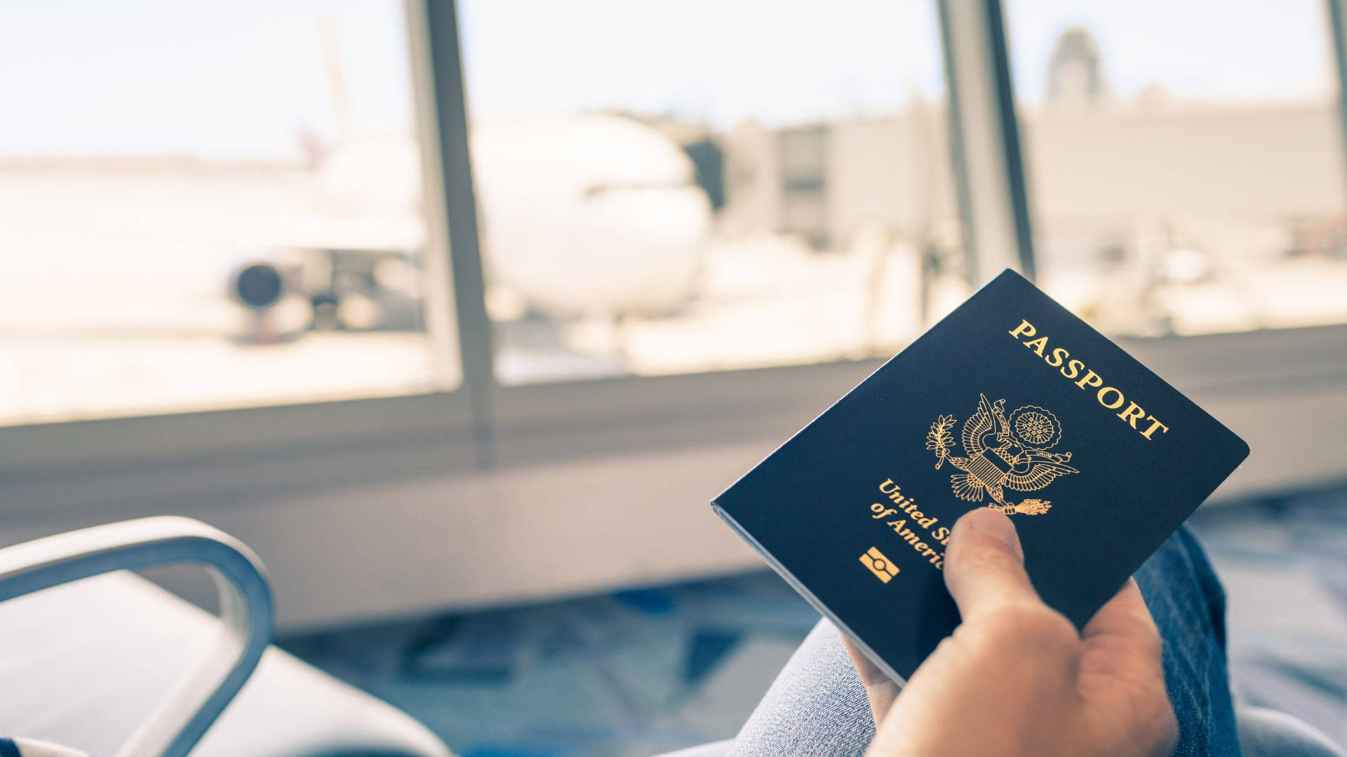 Airport 桌布 壁紙 — 一隻手在機場窗前拿著美國護照，窗外有模糊的飛機。
