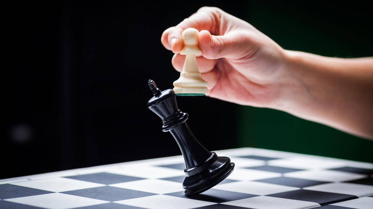西洋棋 桌布 壁紙 — 一隻手在深色背景的棋盤上將白色棋子舉起在倒下的黑色國王之上。
