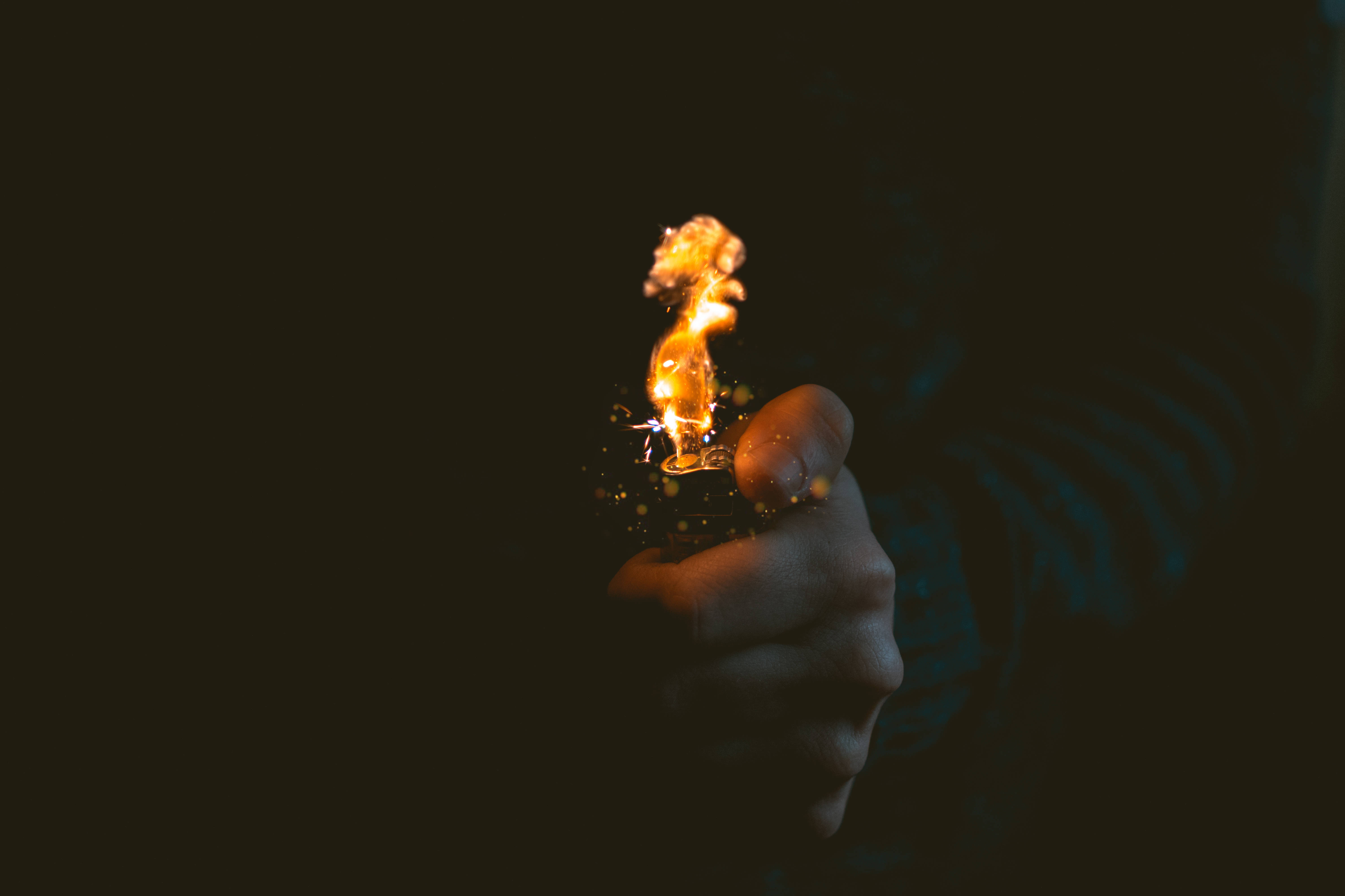 著火 桌布 壁紙 — 一隻手在深黑色背景上抓住閃爍的火焰，投射出溫暖的金色光芒。