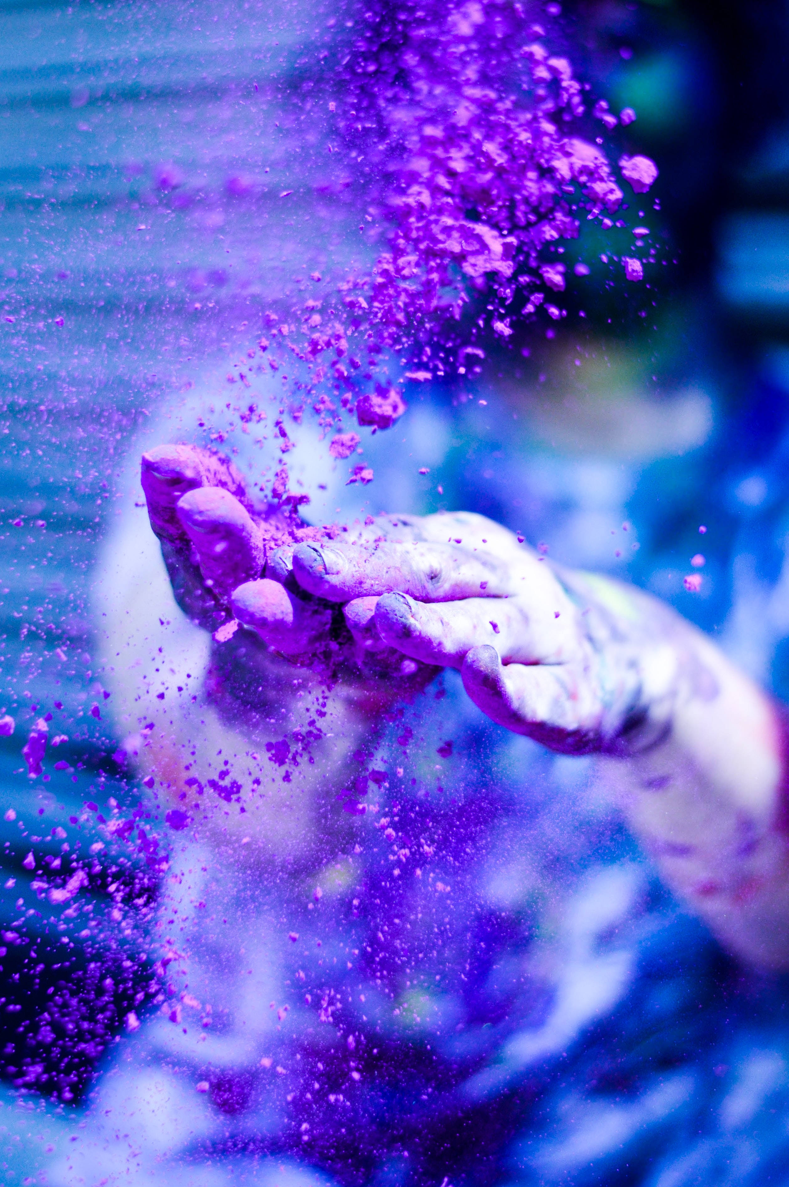 Holi 桌布 壁紙 — 一隻手在清涼的藍色背景上釋放出充滿活力的紫色粉末，形成動態的色彩飛濺。