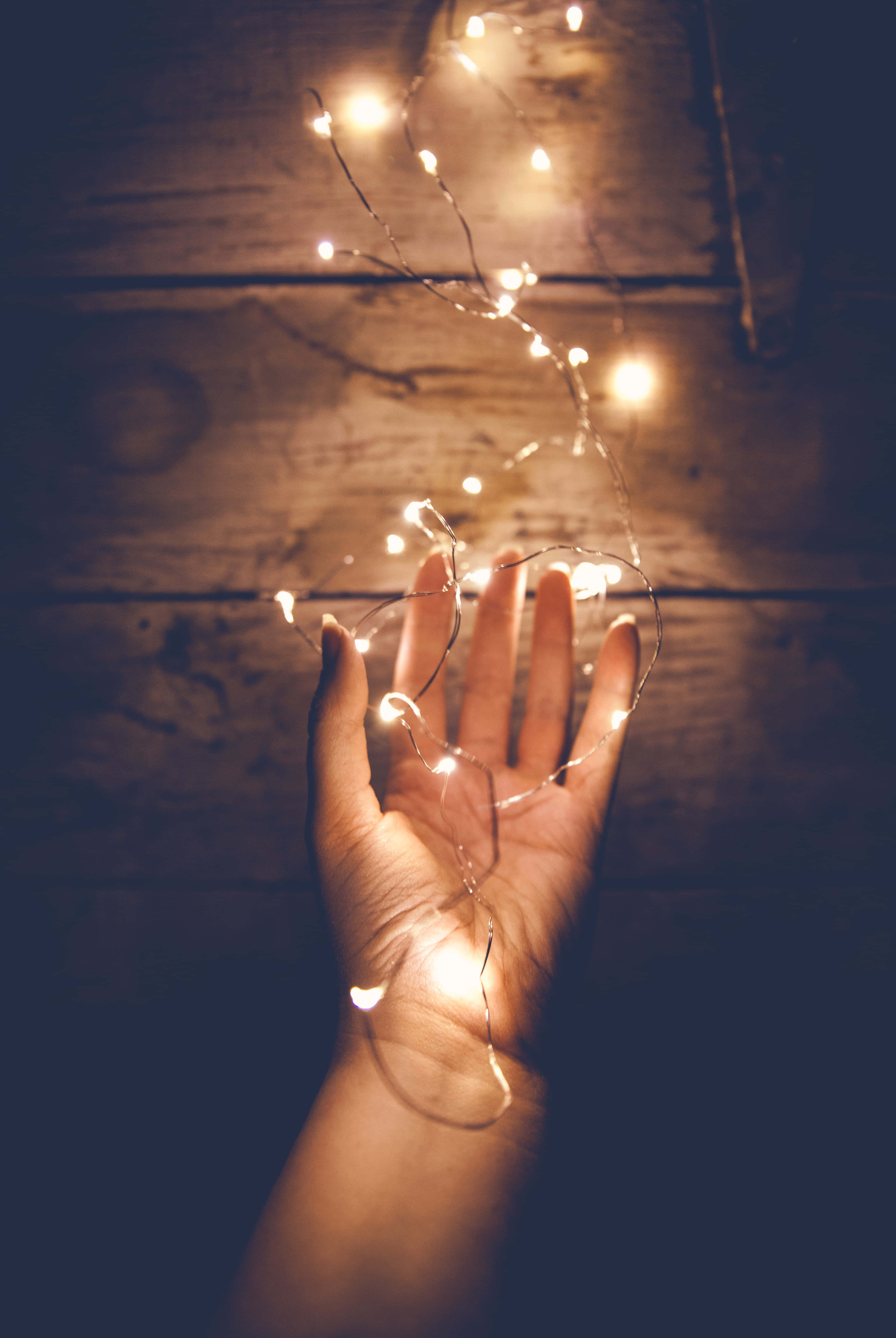 Christmas Light 桌布 壁紙 — 一隻手在溫暖昏暗的光線下，輕輕捧著發光的仙女燈，背景是質樸的木頭。