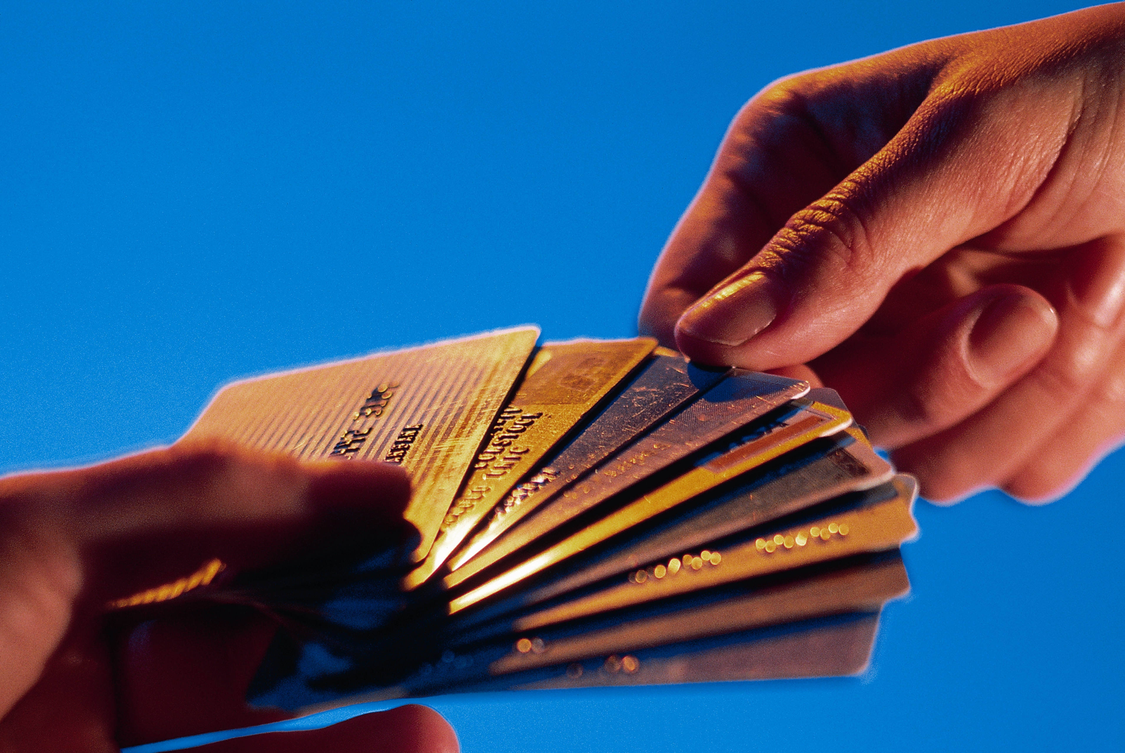 card 桌布 壁紙 — 一隻手在溫暖燈光下，於鮮豔的藍色背景上展開一疊信用卡。