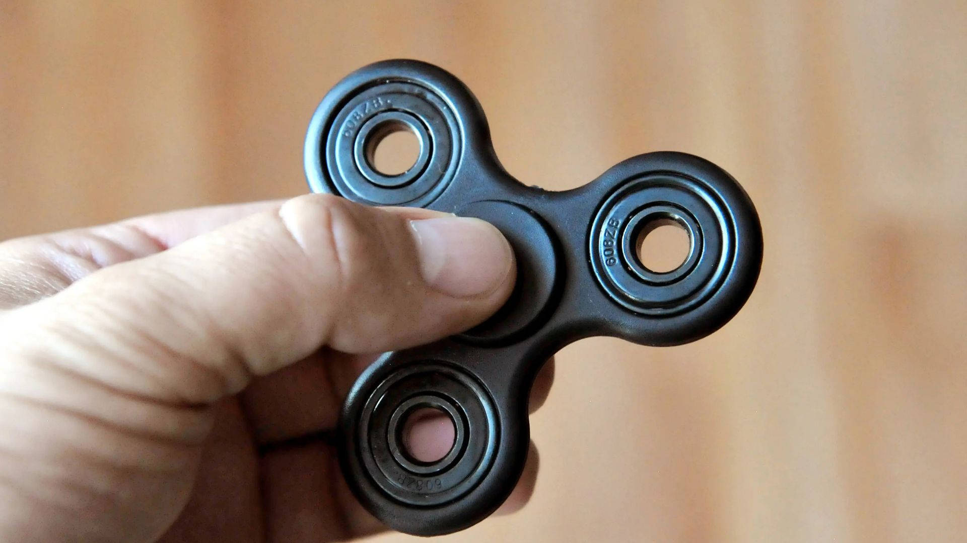 toys 桌布 壁紙 — 一隻手在溫暖的木質背景上拿著一個黑色指尖陀螺，焦點柔和。