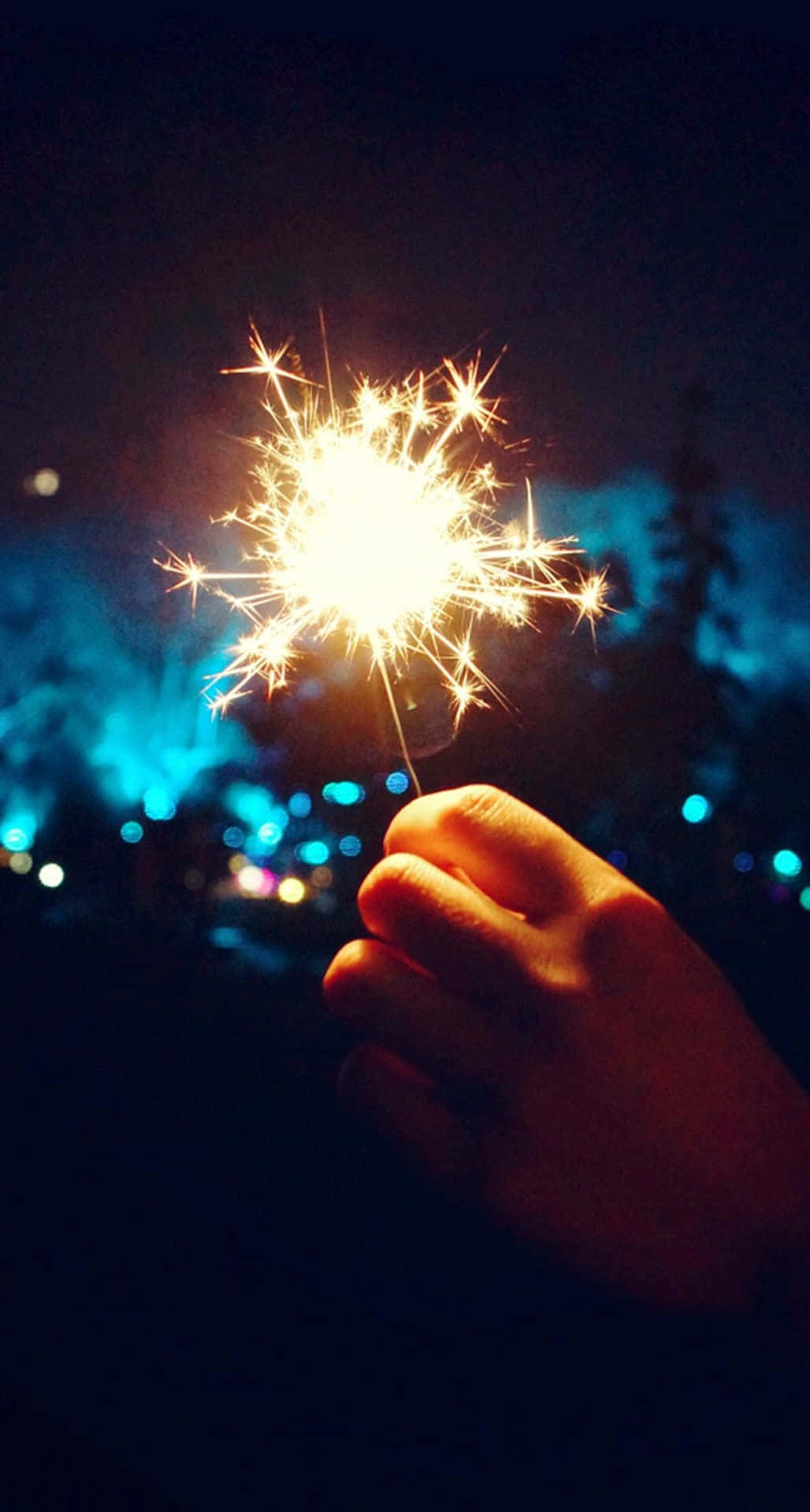 節日 桌布 壁紙 — 一隻手在漆黑的夜空背景下，握著明亮的煙火，背景有藍色散景燈光。