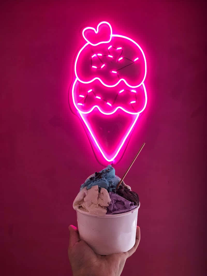 Cute Dessert 桌布 壁紙 — 一隻手在發光的粉紅色霓虹燈牌下，拿著一杯色彩繽紛的冰淇淋，燈牌是兩個冰淇淋球加心形的甜筒形狀。
