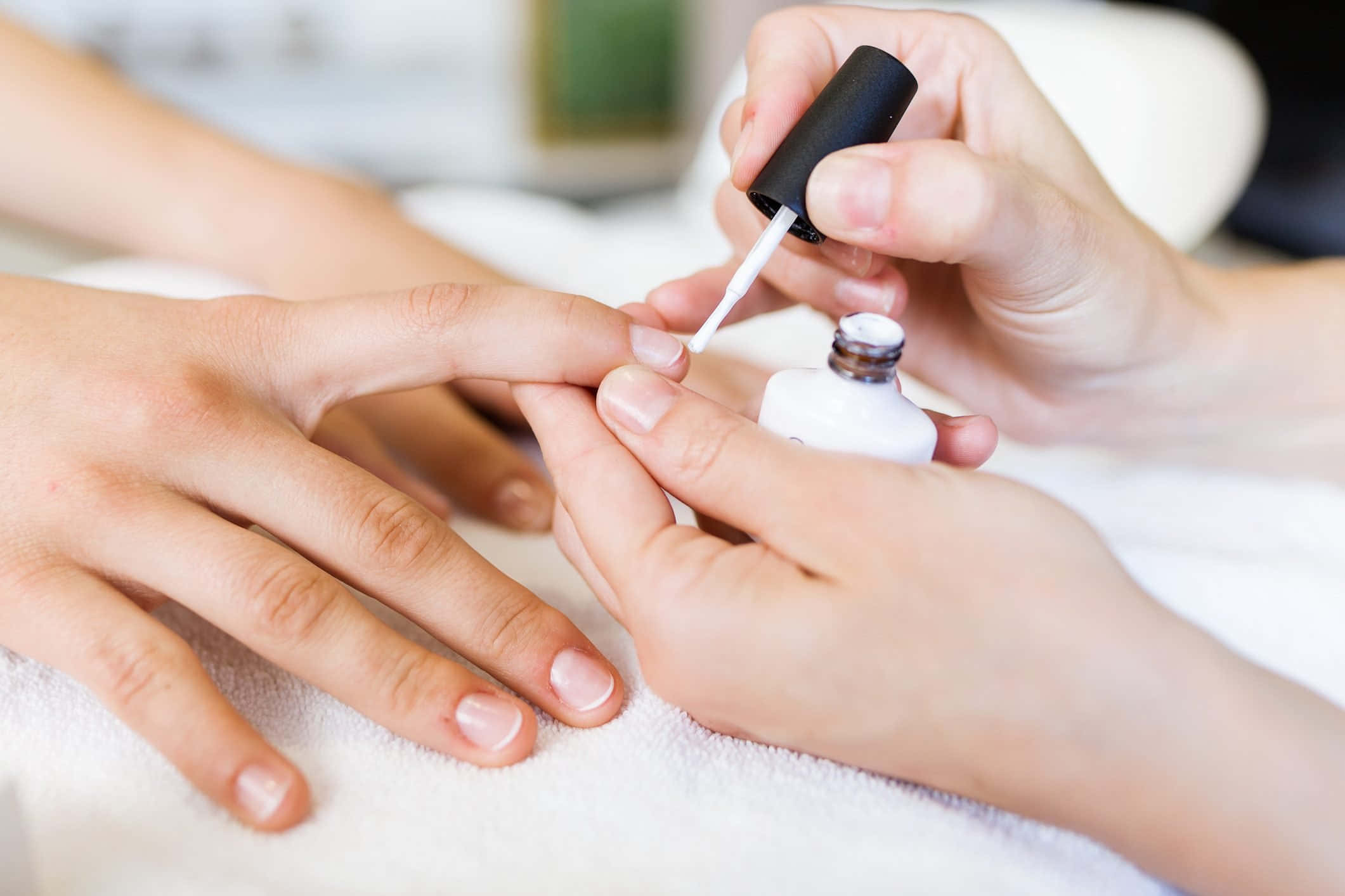 Manicure 桌布 壁紙 — 一隻手在白色毛巾上為另一人的指甲塗上白色指甲油的近距離特寫。