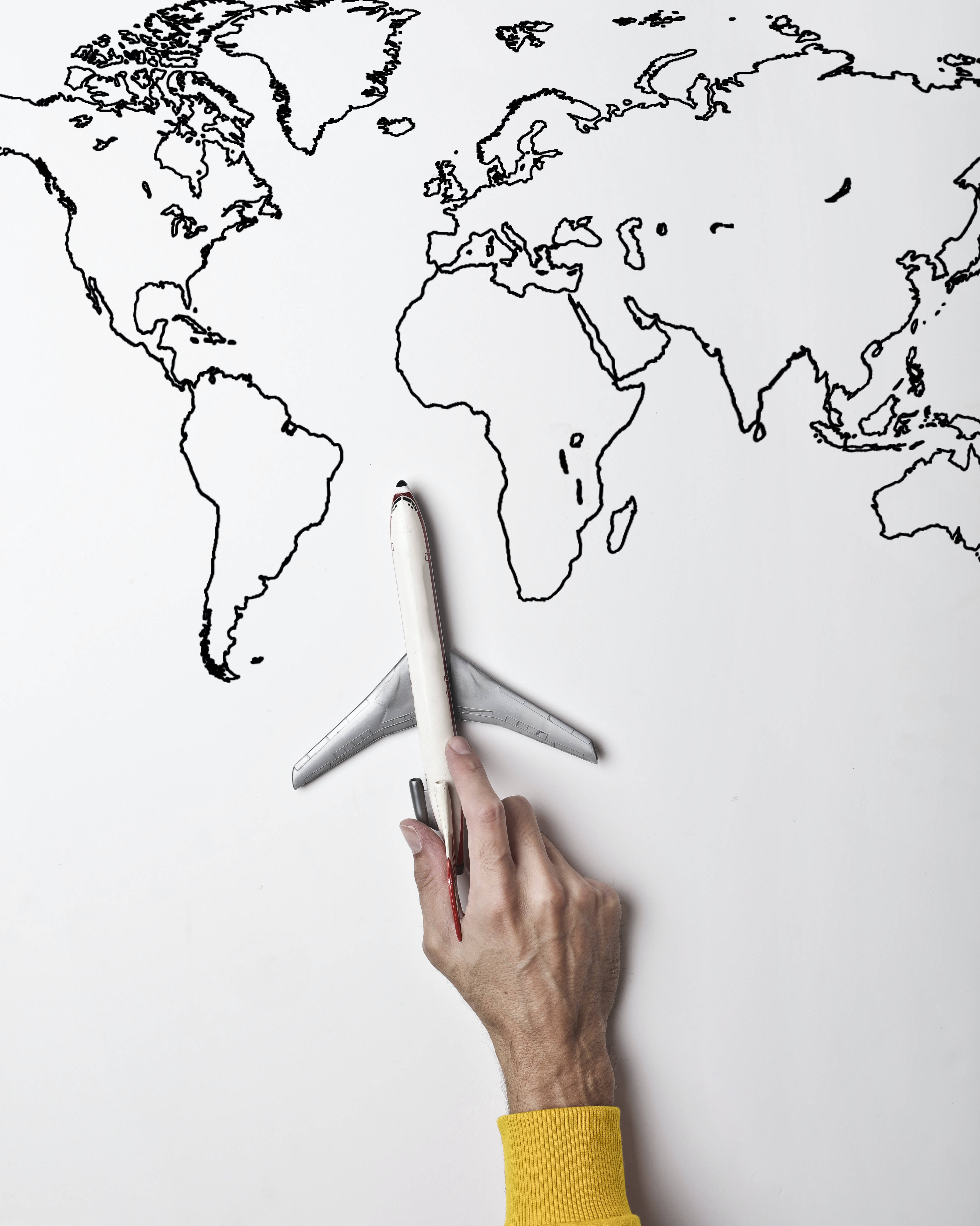 World 桌布 壁紙 — 一隻手在白色紙上的黑色墨水世界地圖上方拿著一個玩具飛機。
