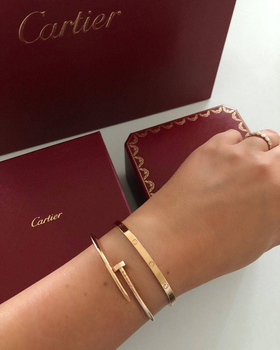 Brand 桌布 壁紙 — 一隻手在白色表面上展示金色Cartier手鐲和戒指，旁邊是優雅的酒紅色品牌盒子。