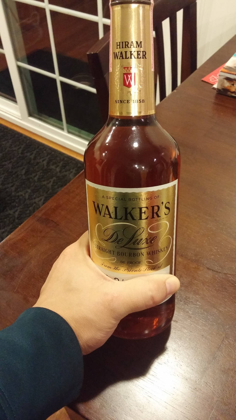alcohol 桌布 壁紙 — 一隻手在窗邊的木桌上拿著一瓶Walker's Deluxe波本威士忌酒瓶。