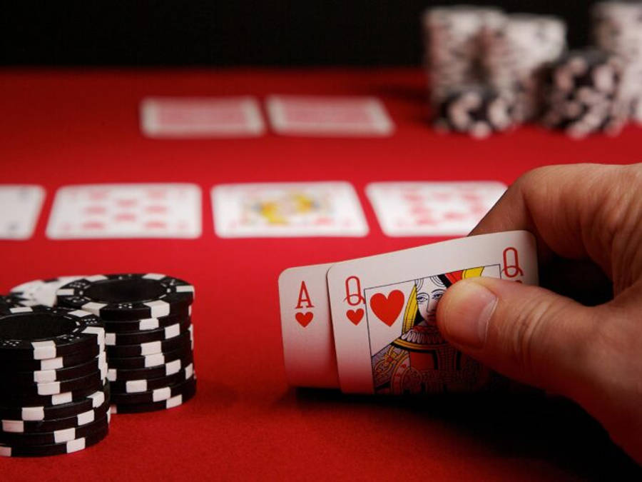 Casino 桌布 壁紙 — 一隻手在紅色撲克桌上拿著A和紅心Q，桌上有成堆的黑色和白色籌碼。