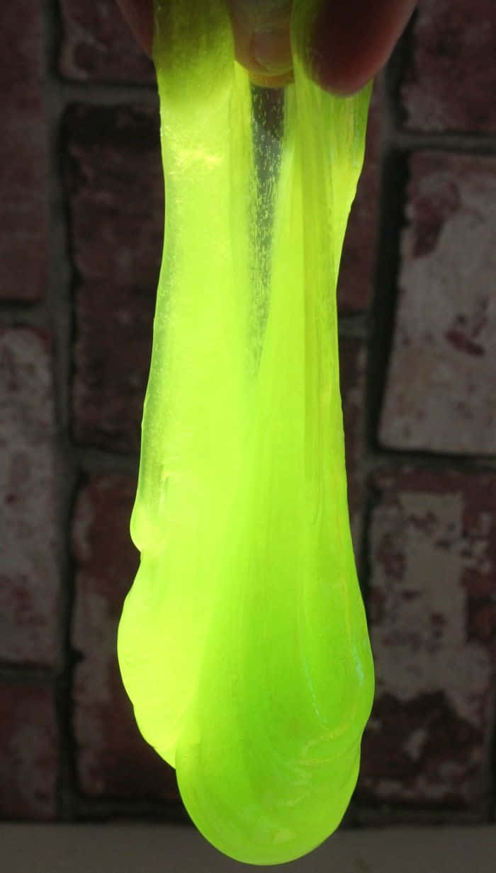 slime 桌布 壁紙 — 一隻手在紋理磚牆背景下拉伸充滿活力的霓虹綠色黏液。