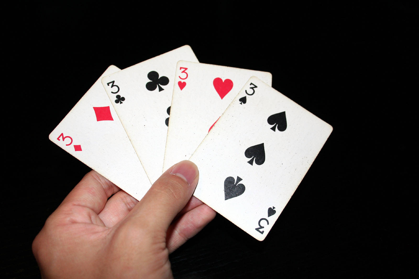 Playing Cards 桌布 壁紙 — 一隻手在純黑背景前攤開四張三條撲克牌。