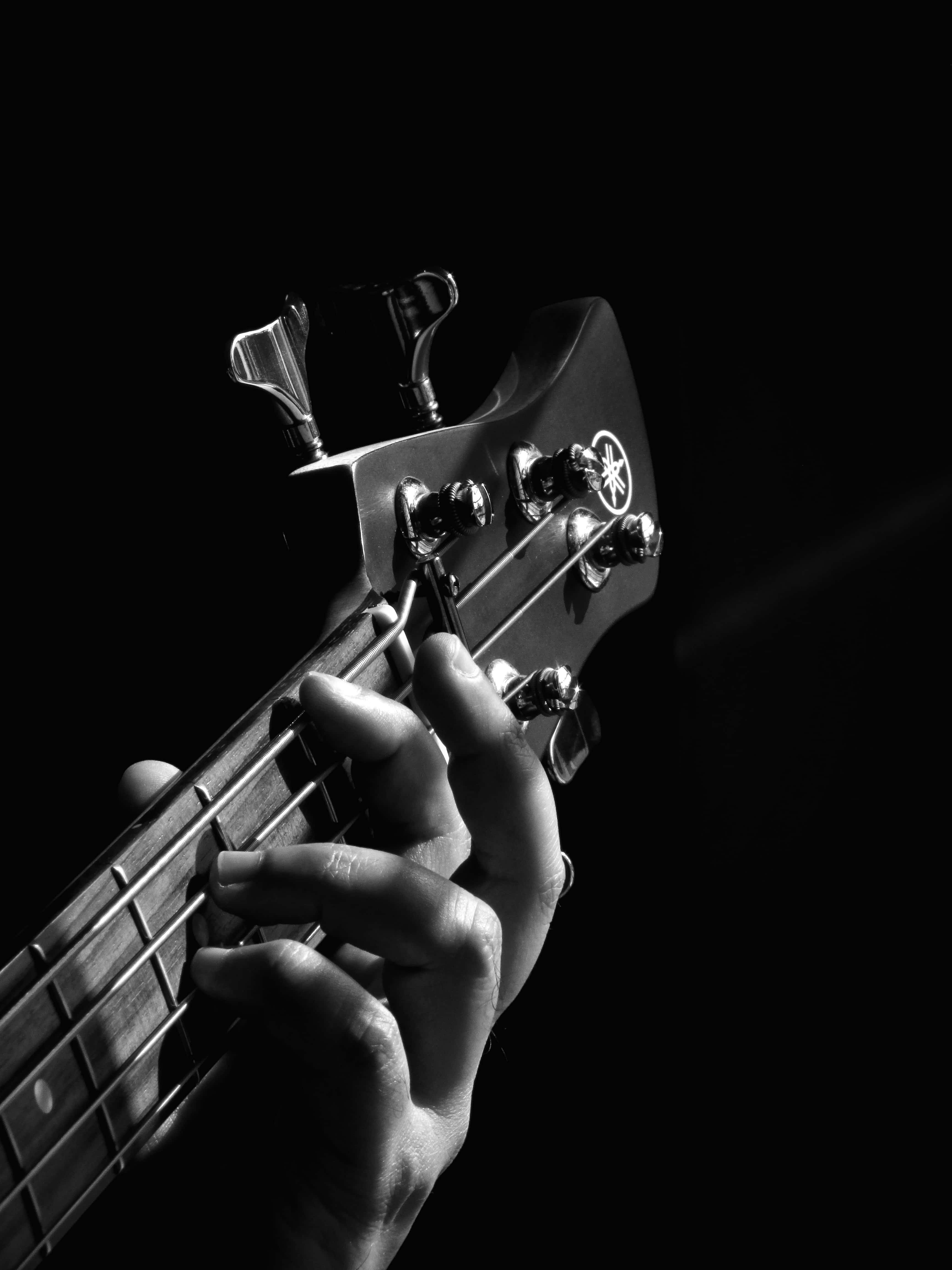 Bass Guitar 桌布 壁紙 — 一隻手在純黑色背景下，於戲劇性的聚光燈下抓住Yamaha低音結他的指板。