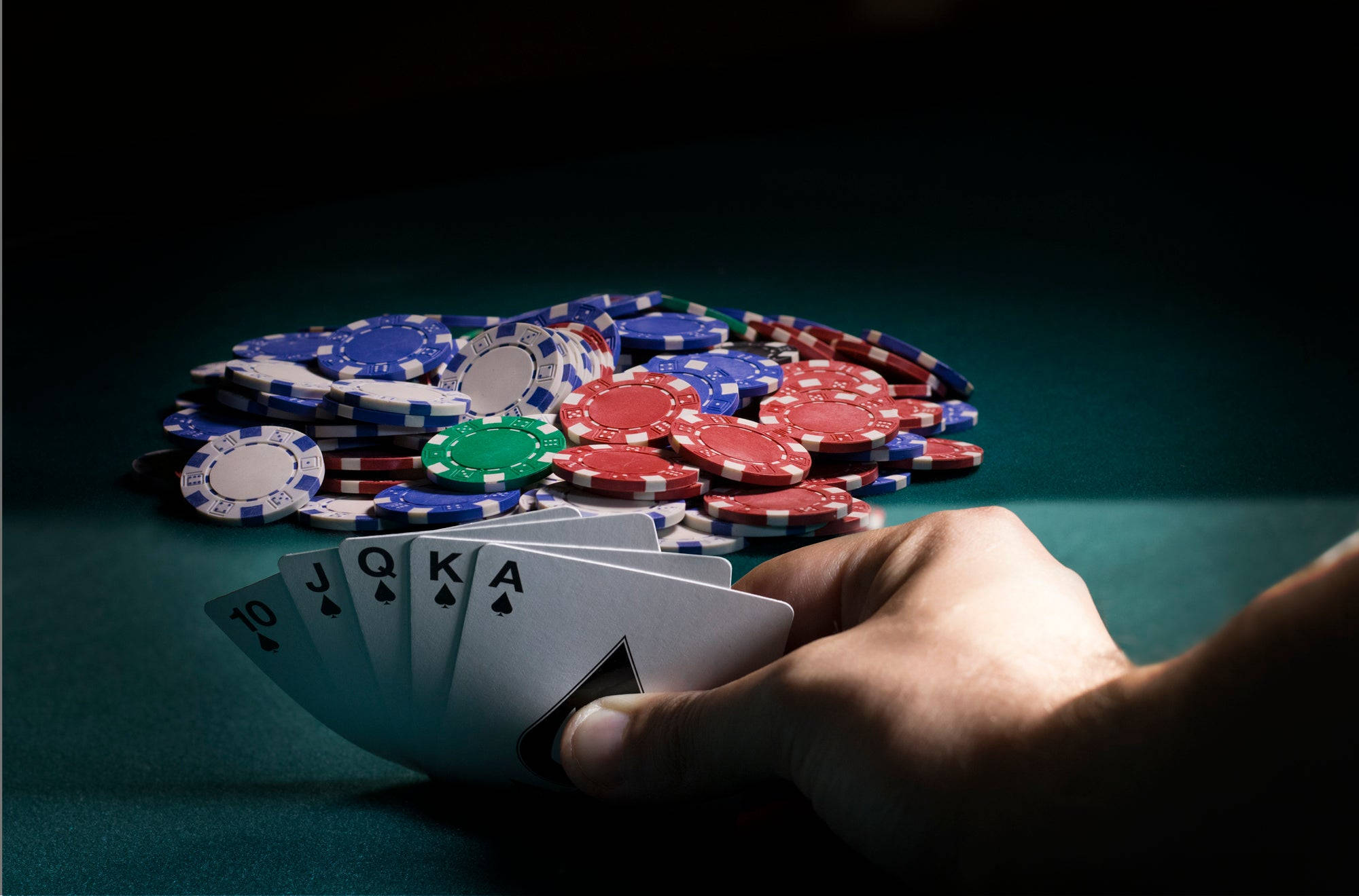 Playing Cards 桌布 壁紙 — 一隻手在綠色氈桌上，在一堆彩色籌碼上方拿著一手贏的撲克牌，是10 J Q K A黑桃。