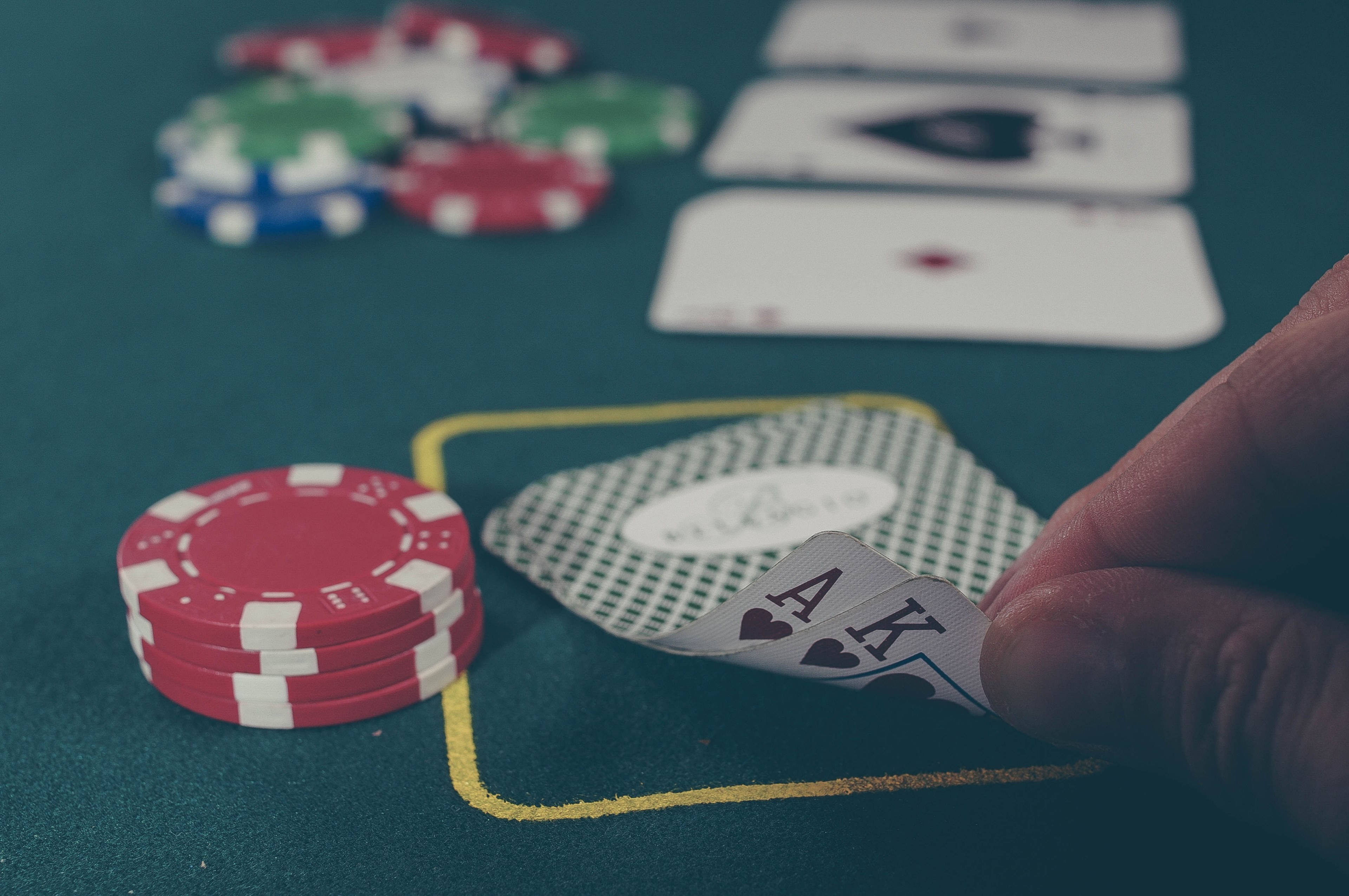 Poker Table 桌布 壁紙 — 一隻手在綠色氈桌上拿著 Ace King 撲克牌，紅色籌碼和其他牌處於柔焦狀態。