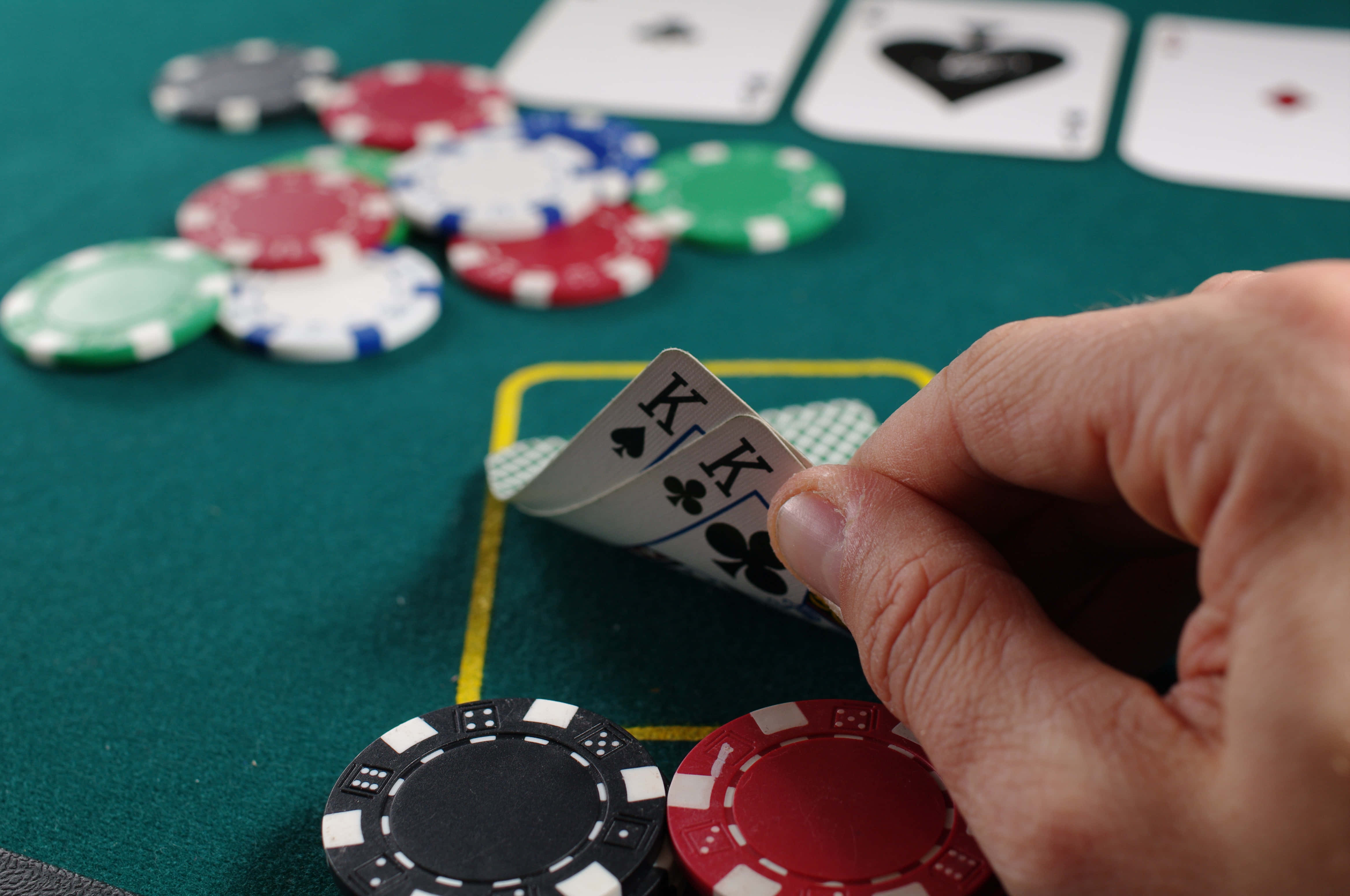 Poker Table 桌布 壁紙 — 一隻手在綠色的撲克牌桌上，桌面散落著彩色籌碼和翻開的撲克牌，手上拿著兩張梅花K。