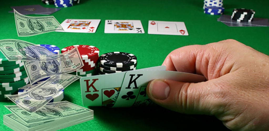 Playing Cards 桌布 壁紙 — 一隻手在綠色絨氈的撲克桌上，周圍堆滿籌碼和現金，揭示兩張K。