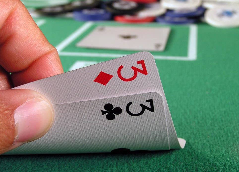 Poker Table 桌布 壁紙 — 一隻手在綠色賭場桌上拿著兩張三點撲克牌，背景有籌碼。