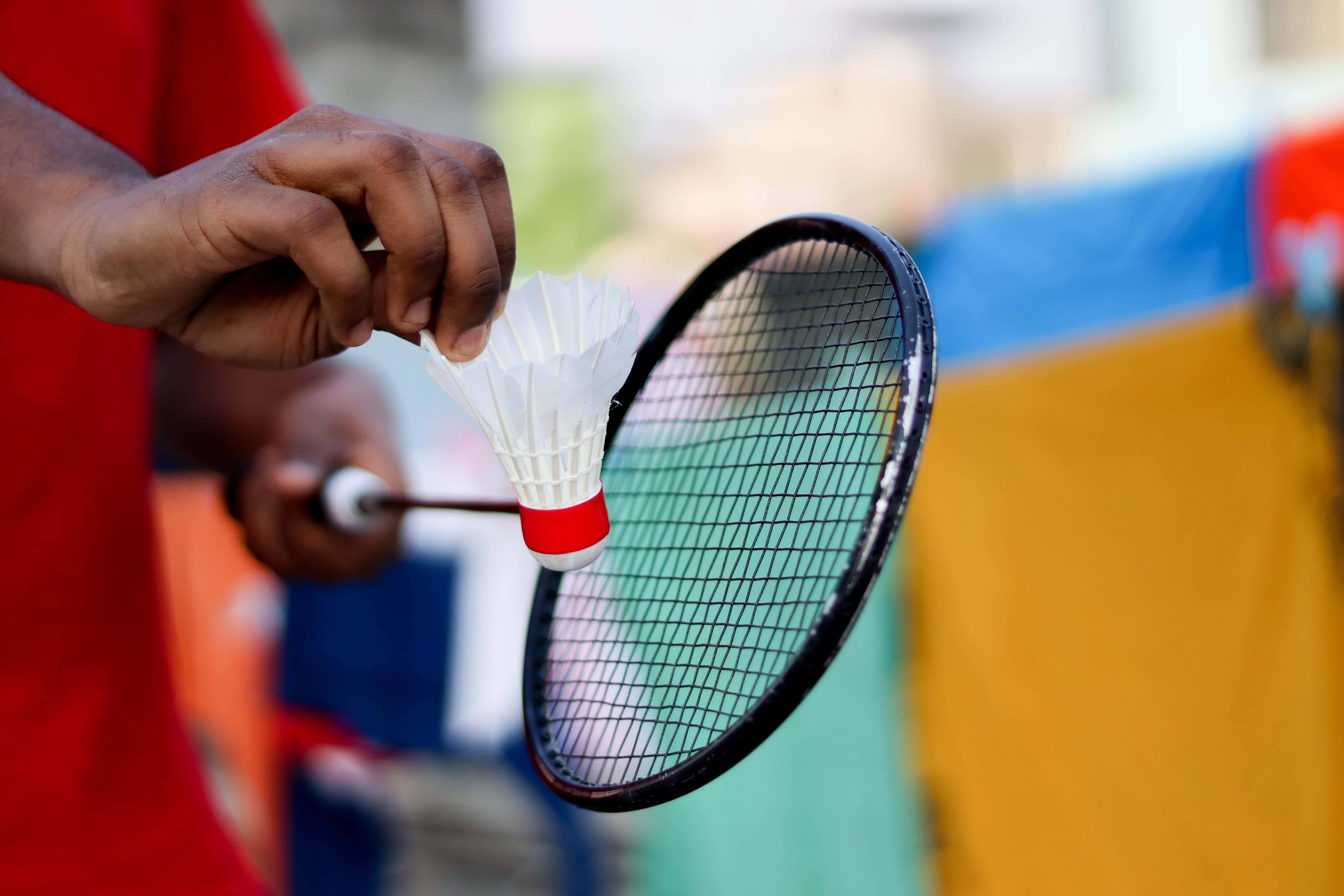 Badminton 桌布 壁紙 — 一隻手在色彩繽紛的模糊背景前，在球拍附近握住羽毛球的特寫。