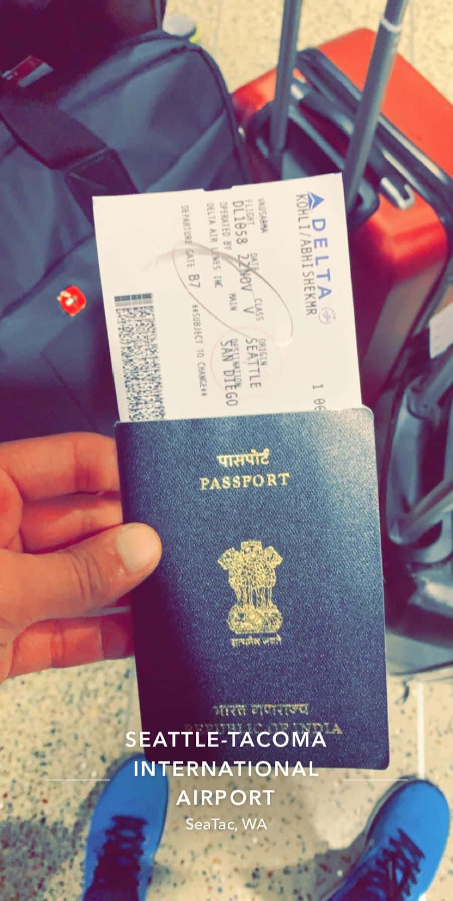 Passport 桌布 壁紙 — 一隻手在西雅圖-塔科馬國際機場拿著印度護照和達美航空登機證，行李和藍色運動鞋可見。