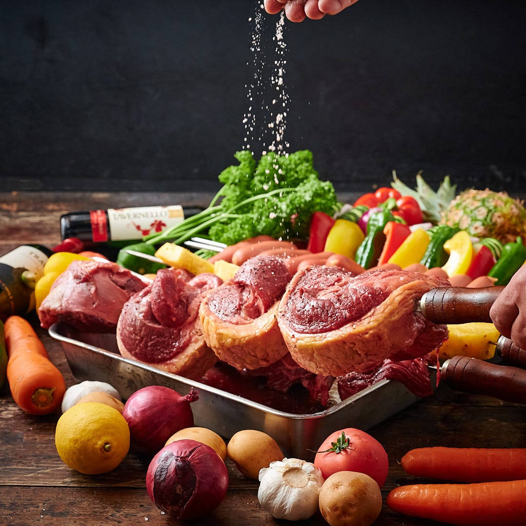 meat 桌布 壁紙 — 一隻手在質樸的木桌上，將鹽撒在被色彩繽紛的新鮮蔬菜包圍的生牛肉烤肉上。