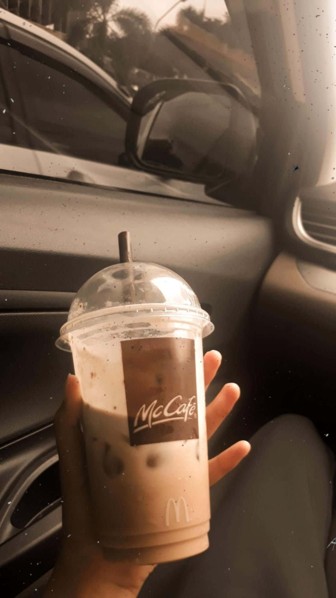 Mcdonalds 桌布 壁紙 — 一隻手在車內拿著McCafé冰咖啡，溫暖的陽光透過窗戶照射進來。