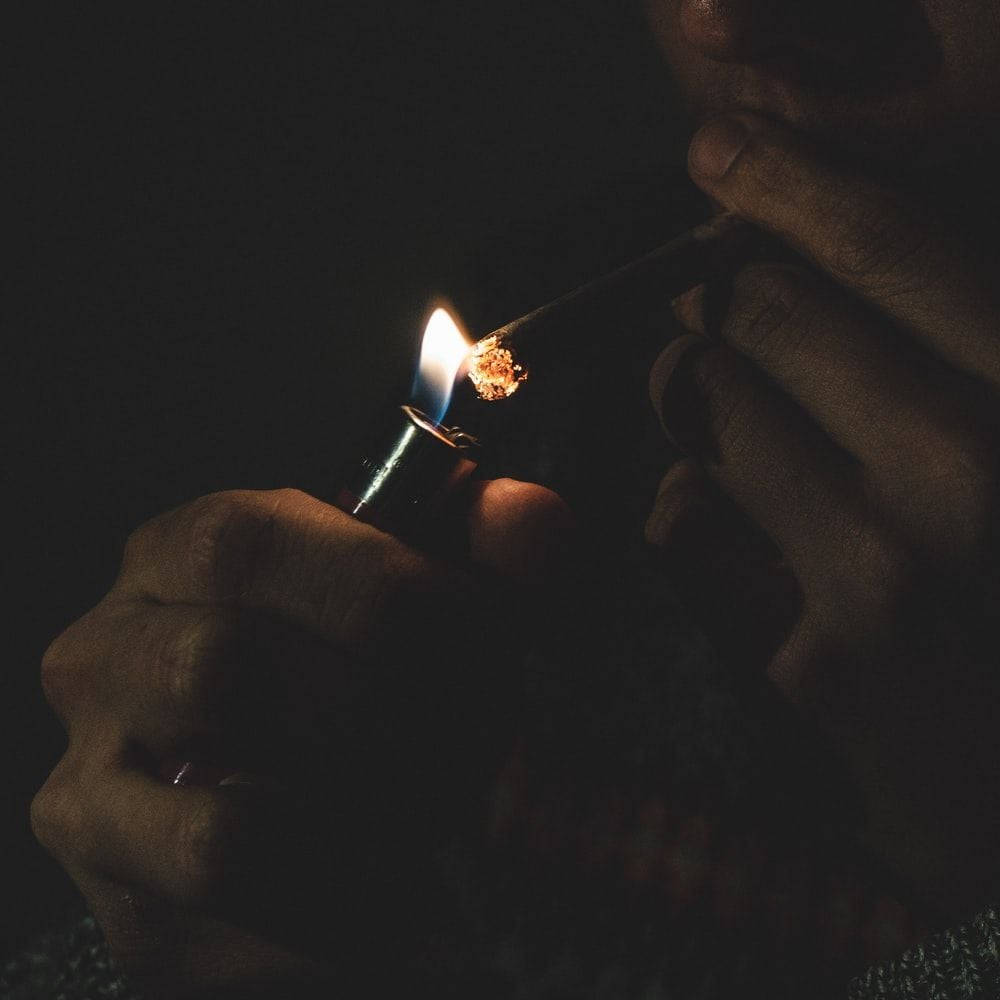 Blunt 桌布 壁紙 — 一隻手在近乎黑暗中用打火機點燃一支大麻煙，在手指和煙霧上投射出溫暖的光芒。