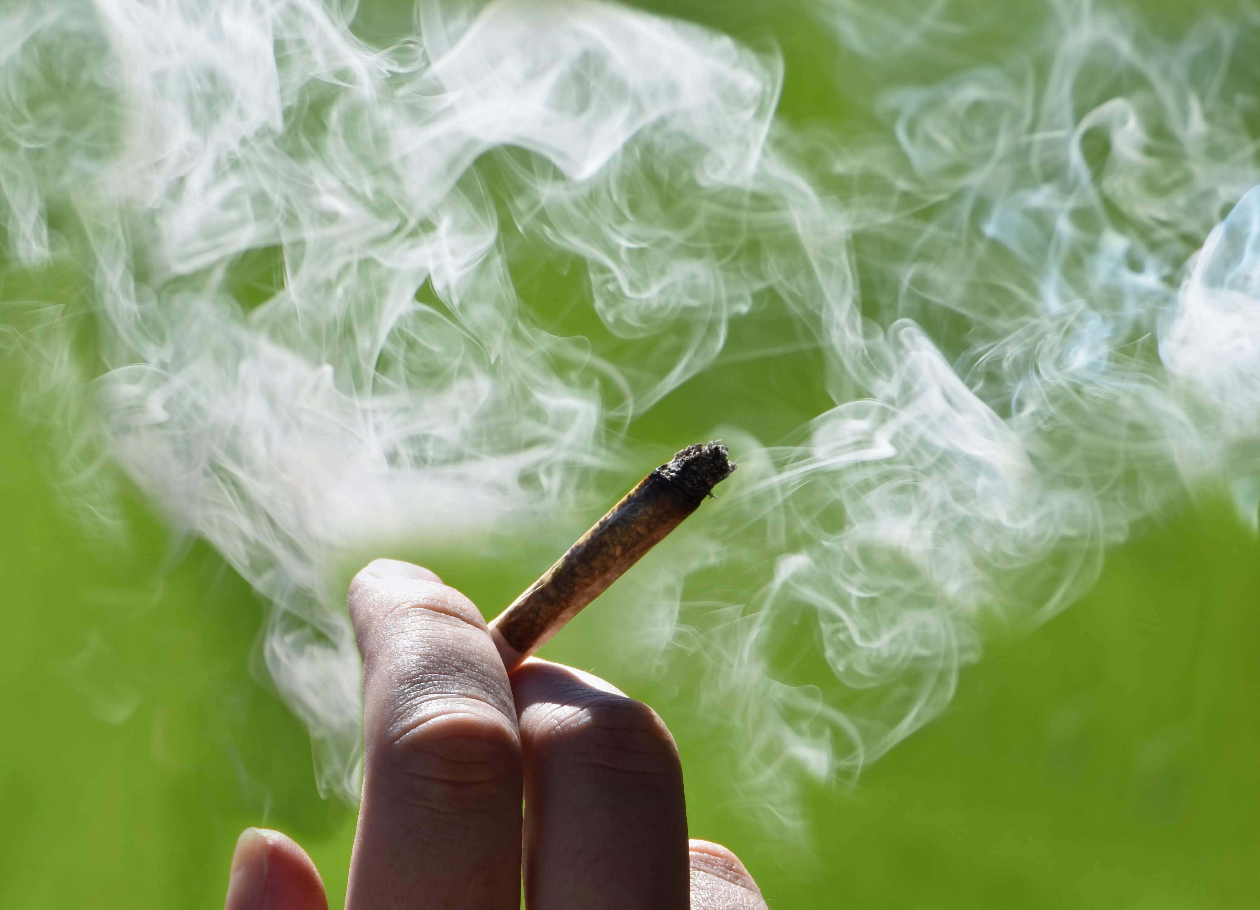 Weed Blunt 桌布 壁紙 — 一隻手在鮮綠色背景前拿著一支點燃的大麻煙，濃厚的白煙向上盤旋。