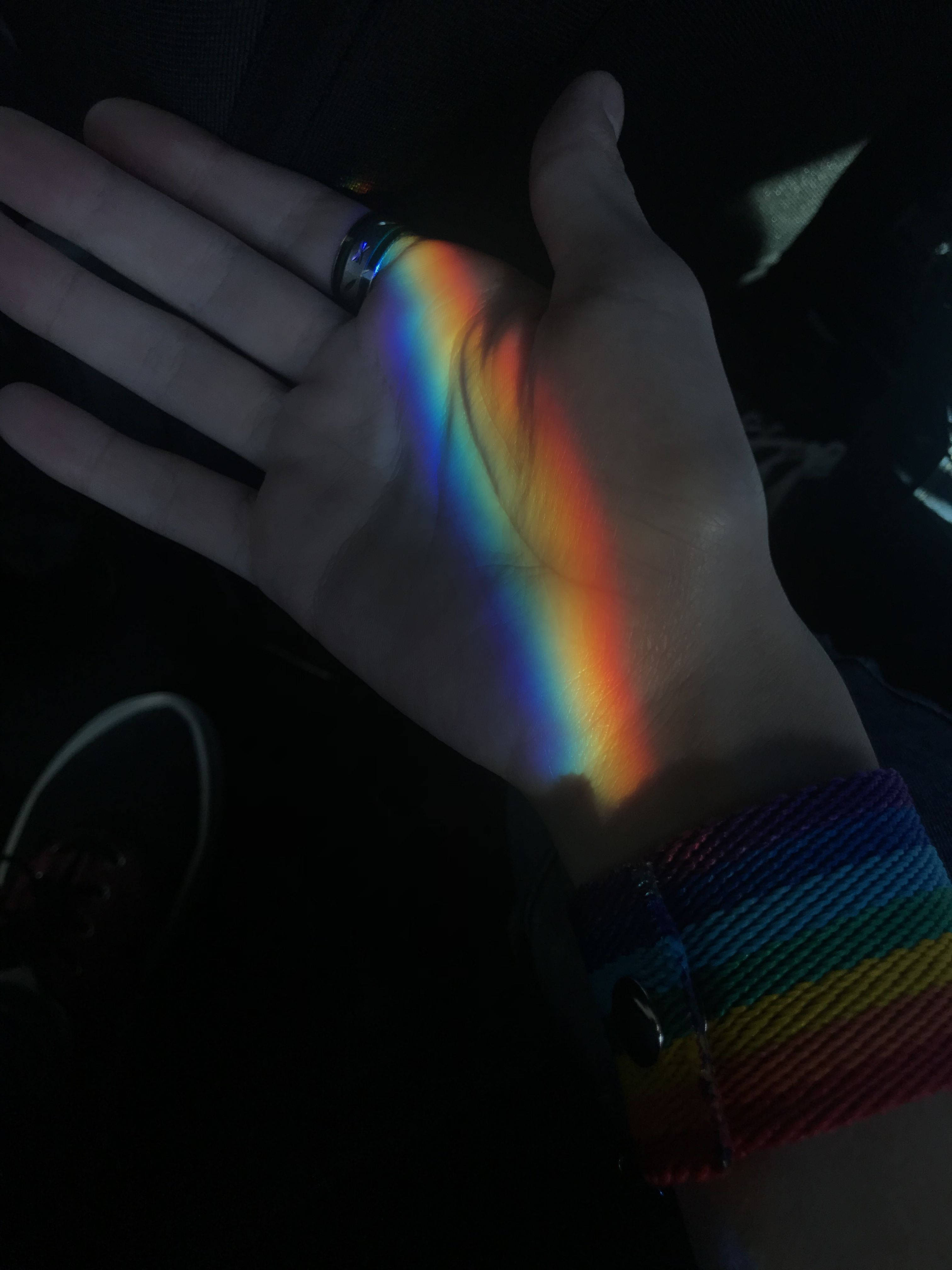 LGBT 桌布 壁紙 — 一隻手在黑暗中拿著鮮豔的彩虹光投影，戴著彩虹手環和戒指。