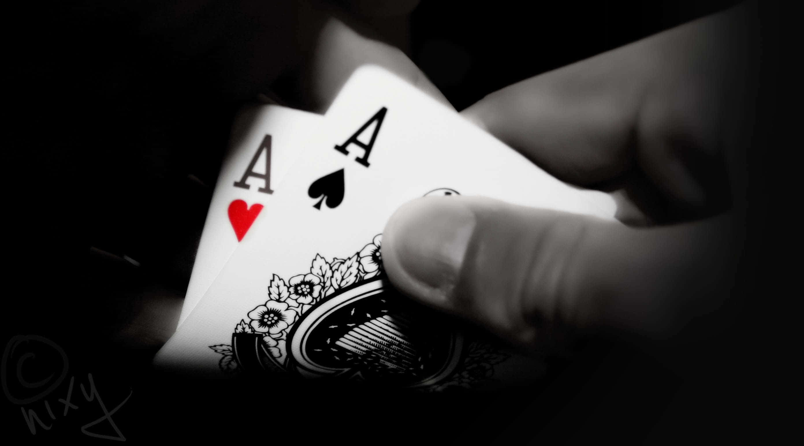 Poker 桌布 壁紙 — 一隻手在黑色背景的戲劇性聚光燈下拿著兩張紅心和黑桃的Ace。