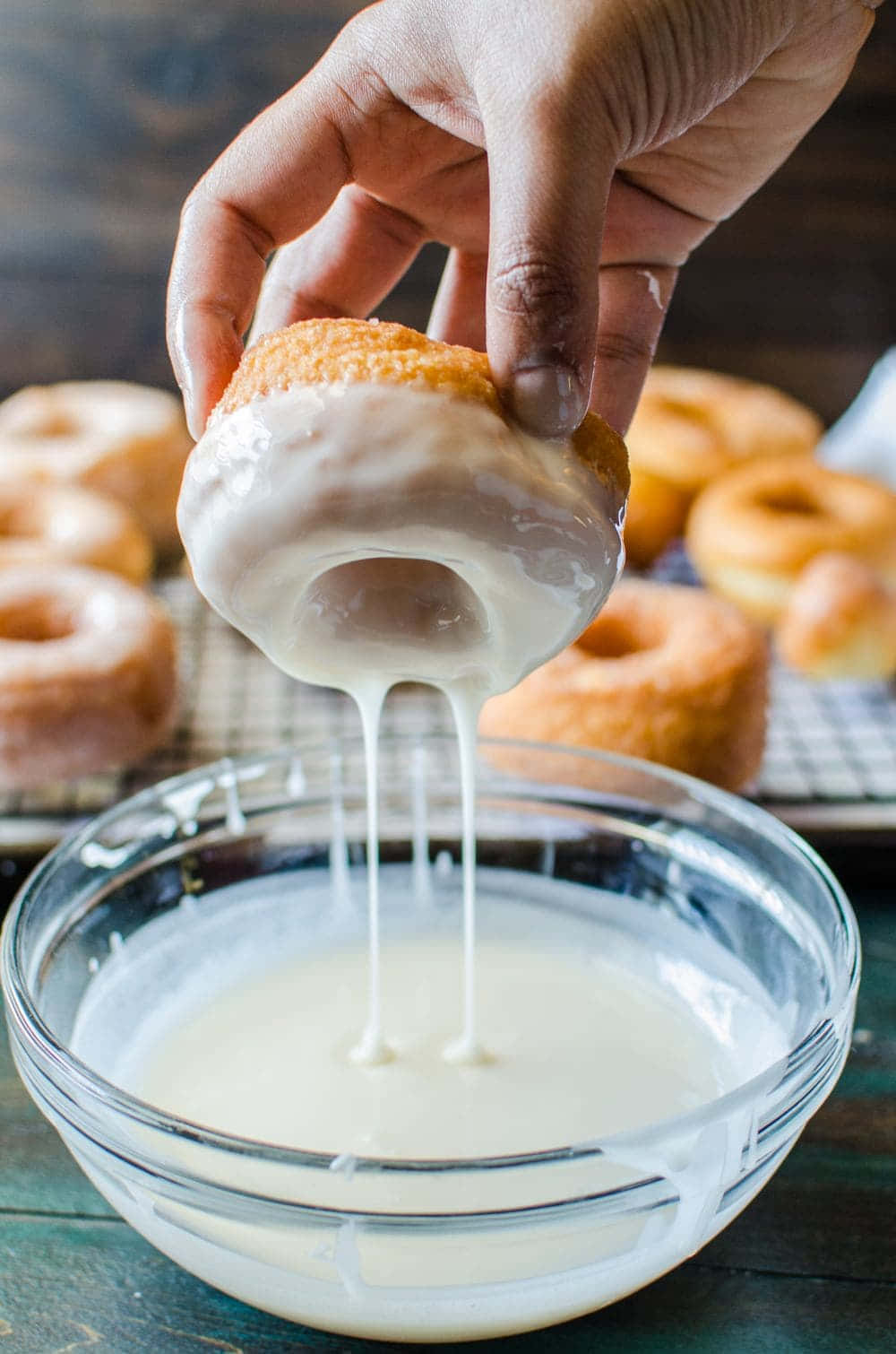 Glazed Donut 桌布 壁紙 — 一隻手將一個金色甜甜圈浸入一碗奶油狀的白色糖霜中，濃稠的滴落物回落到碗中。