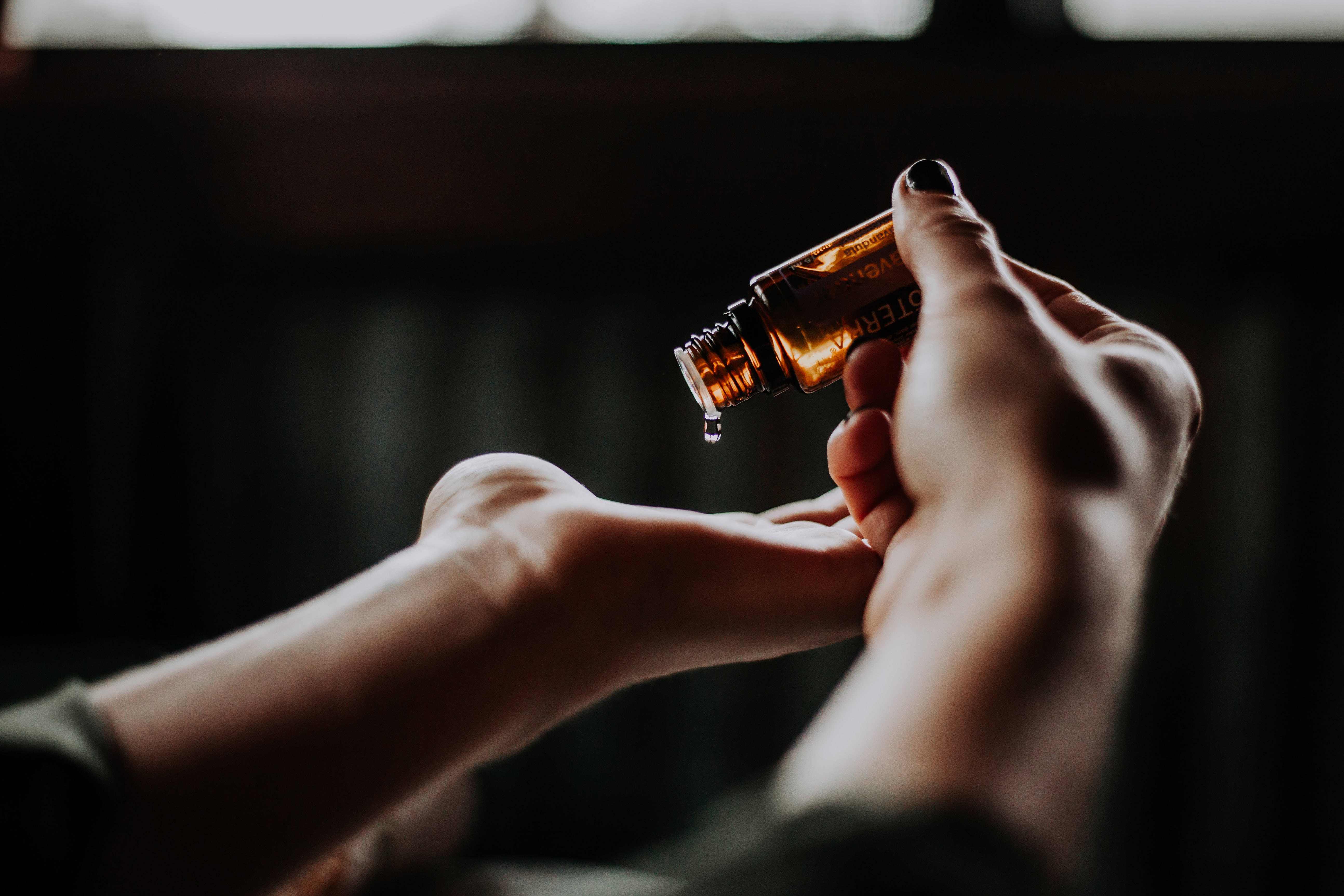 hand 桌布 壁紙 — 一隻手將一滴琥珀色精油滴在另一隻手上，環境昏暗而親密。