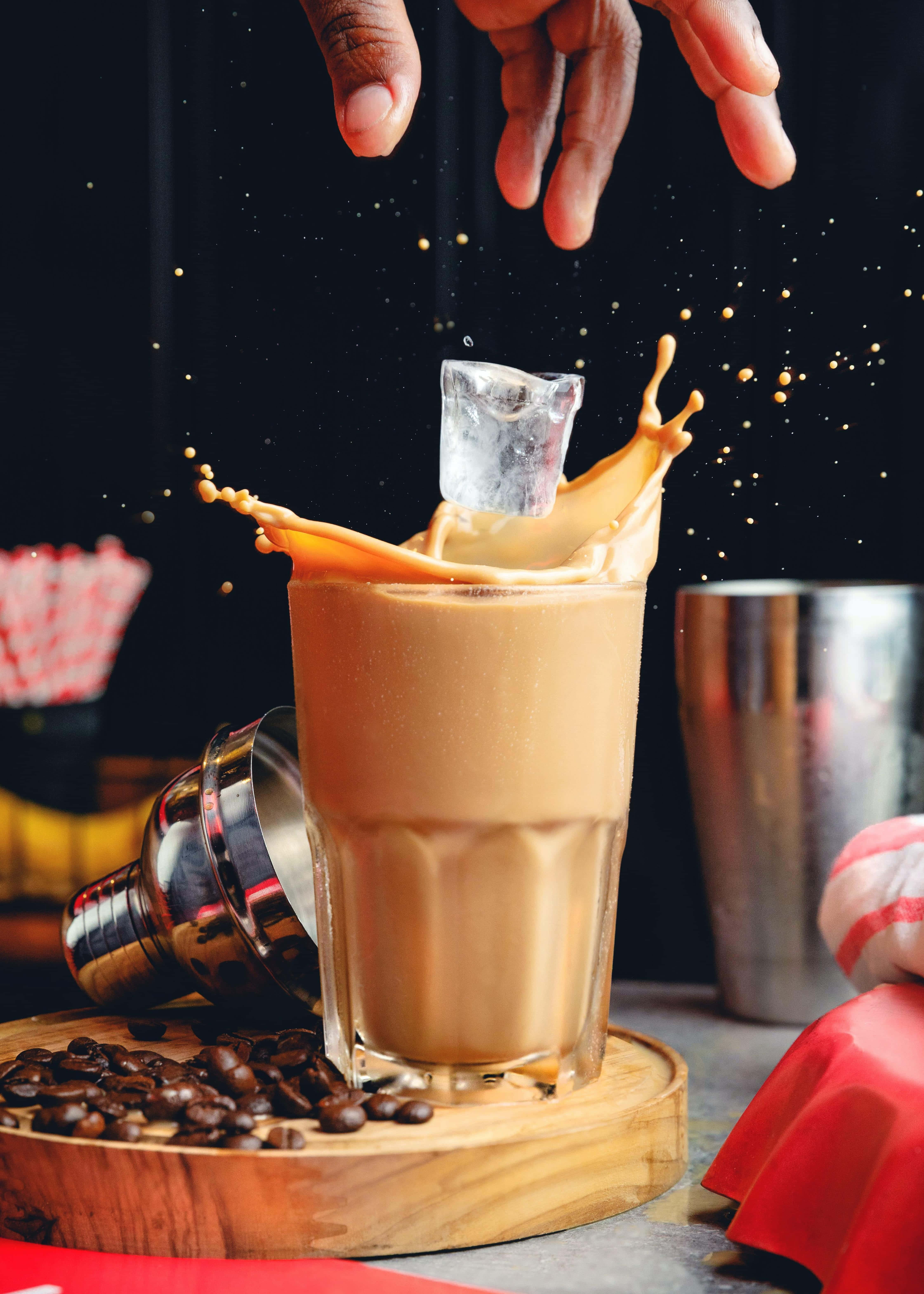 Iced Coffee 桌布 壁紙 — 一隻手將冰塊放入奶油咖啡飲料中，在深色背景上引起金色飛濺。