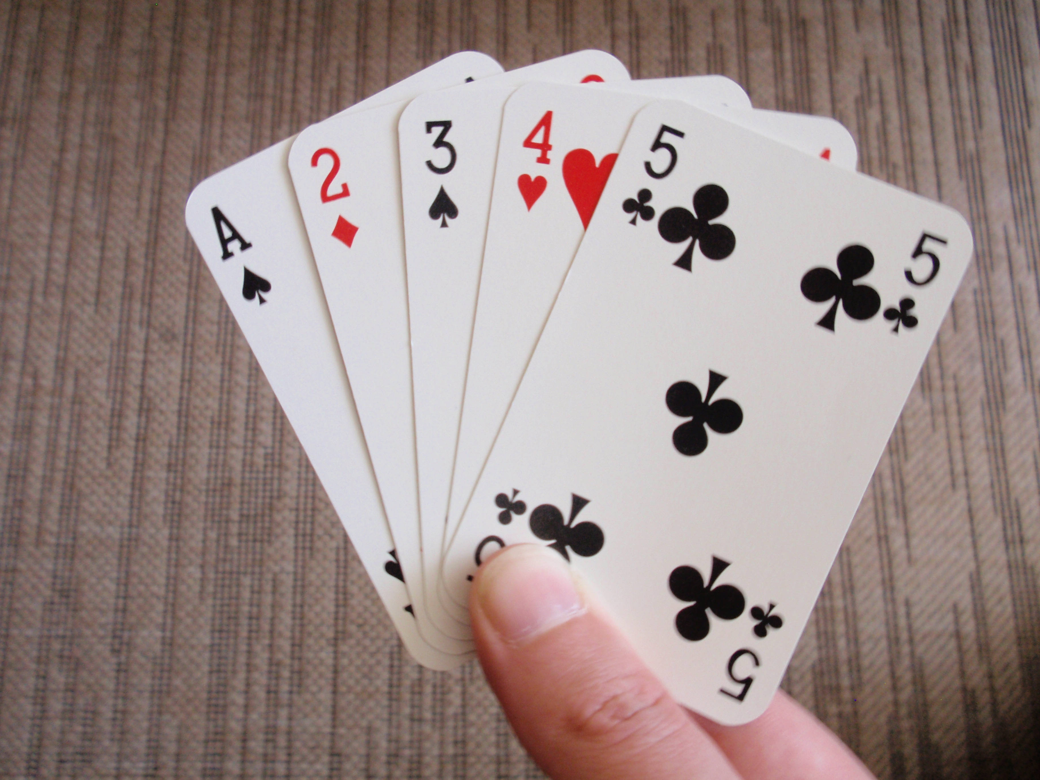 Casino 桌布 壁紙 — 一隻手將撲克牌扇開，展示A、2、3、4、5，背景為有紋理的布料。