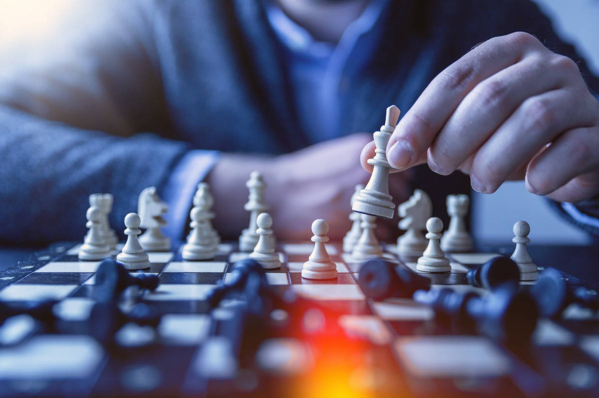 西洋棋 桌布 壁紙 — 一隻手將白色國王棋提起，下方棋盤上有倒下的黑色棋子及發光的紅光特寫。