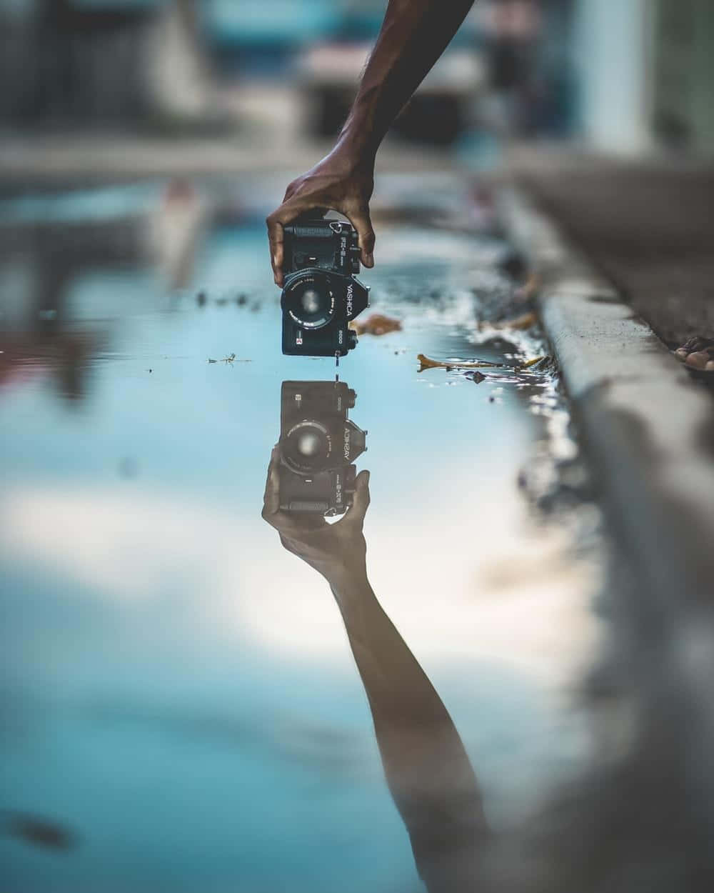 Dslr 桌布 壁紙 — 一隻手將相機舉在水坑上方，營造出場景完美的鏡像倒影。