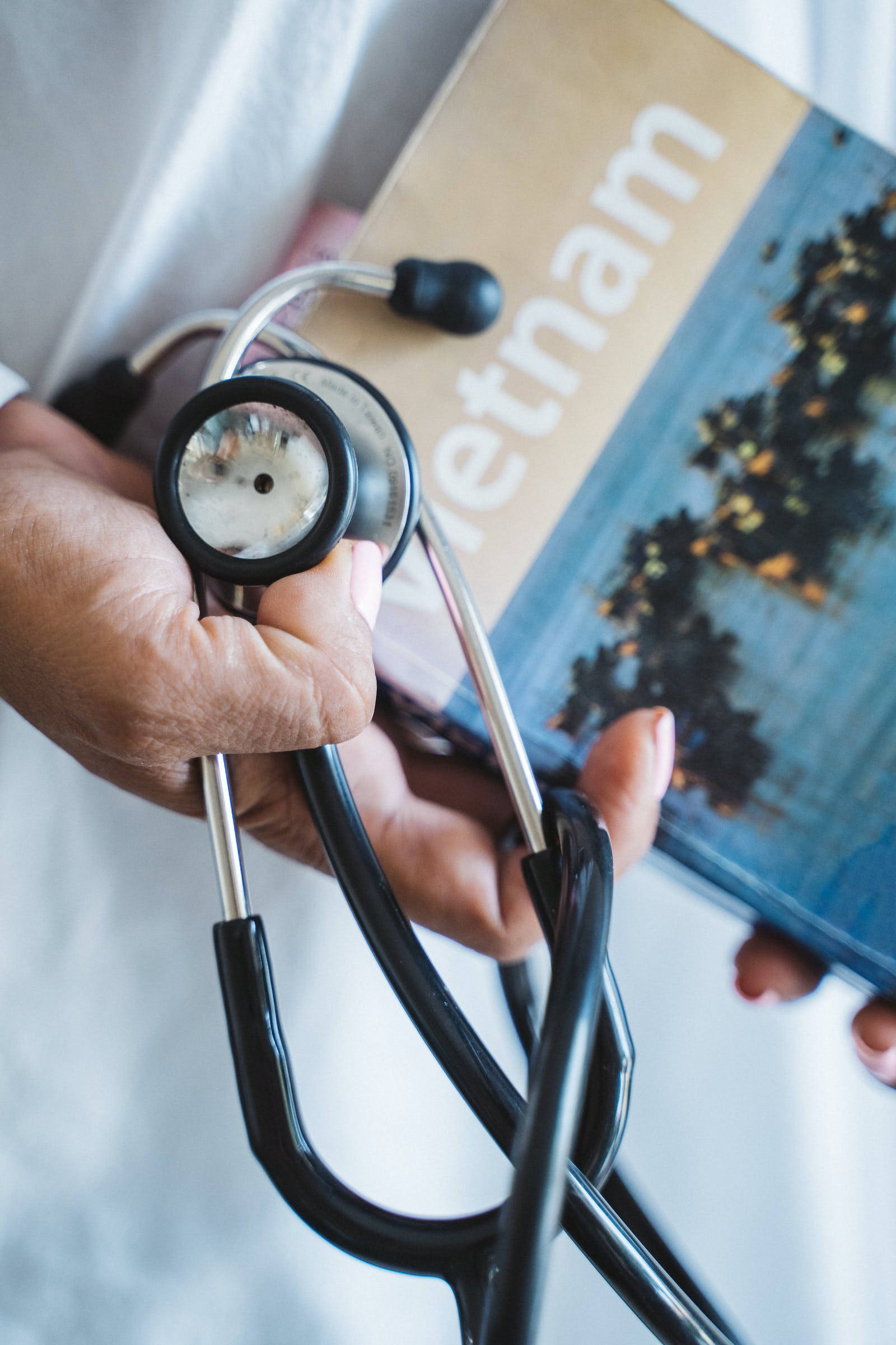 doctor motivation 桌布 壁紙 — 一隻手將聽診器放在一本名為「越南」的旅遊指南上，封面是模糊的城市景觀。