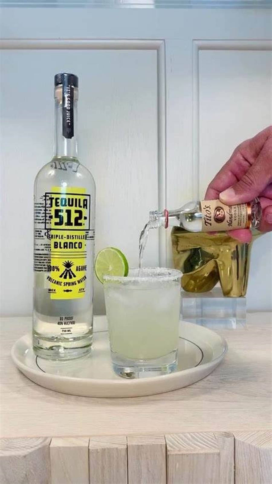 drinks 桌布 壁紙 — 一隻手將龍舌蘭酒倒入一個鹽邊瑪格麗特杯中，旁邊放著一瓶Tequila 512 Blanco，置於木質檯面上。
