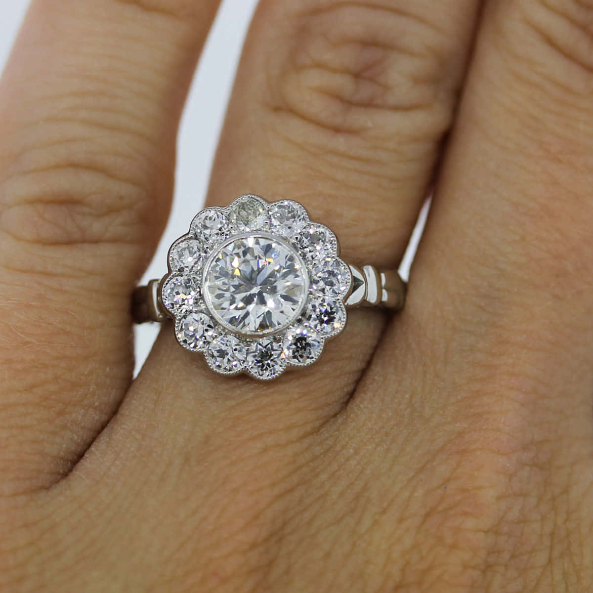 rings 桌布 壁紙 — 一隻手展示了一枚復古風格的鑽石戒指，中央圓形主石周圍環繞著一圈較小的鑽石。