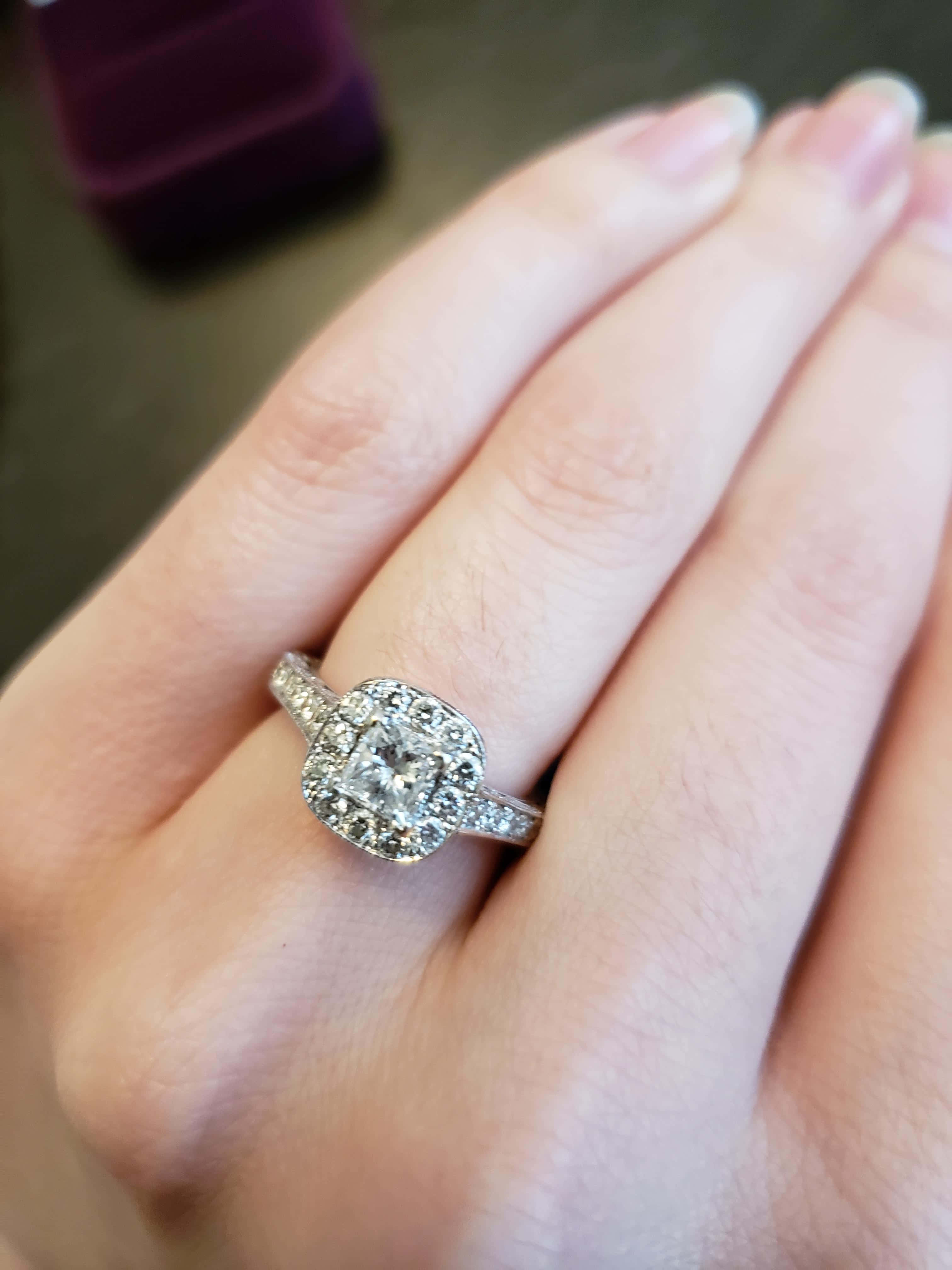rings 桌布 壁紙 — 一隻手展示了一枚閃閃發光的鑽石訂婚戒指，採用 cushion cut 主石和 halo 鑲嵌。
