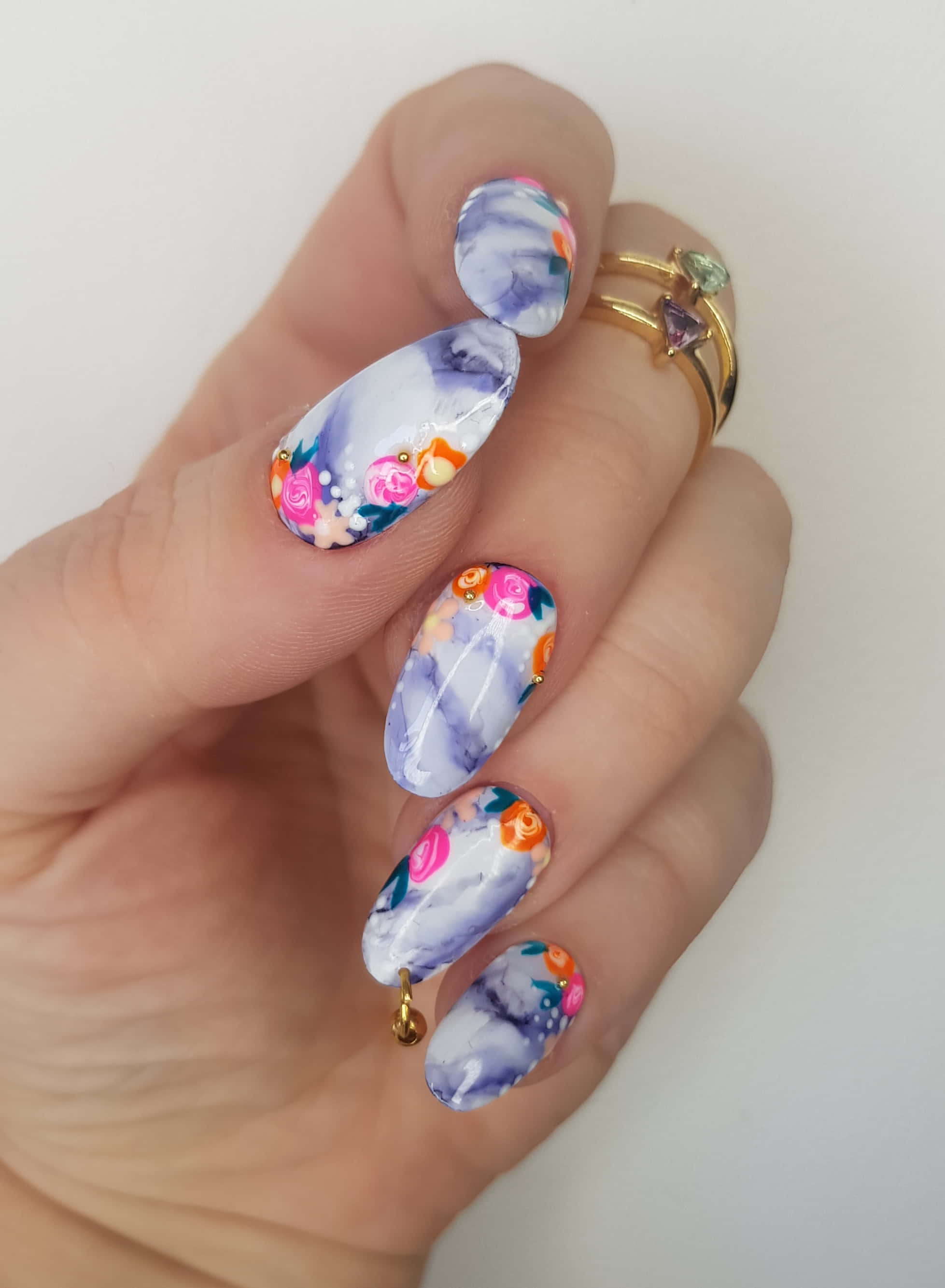 Spring Nails 桌布 壁紙 — 一隻手展示設計精緻的指甲，帶有紫色大理石和色彩繽紛的花卉圖案，並以金色珠子點綴。
