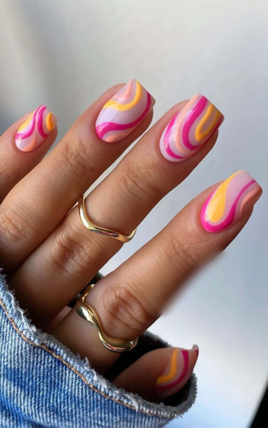Nail 桌布 壁紙 — 一隻手帶有充滿活力的粉紅、黃和白漩渦指甲藝術，戴著金戒指和牛仔布袖。