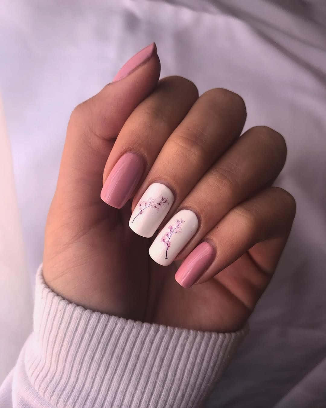Pink Nails 桌布 壁紙 — 一隻手帶有柔軟的粉紅色和白色指甲，飾有精緻的櫻花圖案，輕輕放在白色羅紋毛衣袖子上。