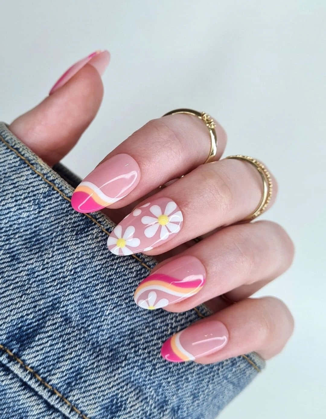 Pink Nail Art 桌布 壁紙 — 一隻手帶有粉彩粉紅色指甲，飾有白色雛菊和波浪形粉橙色條紋，放在牛仔布上。