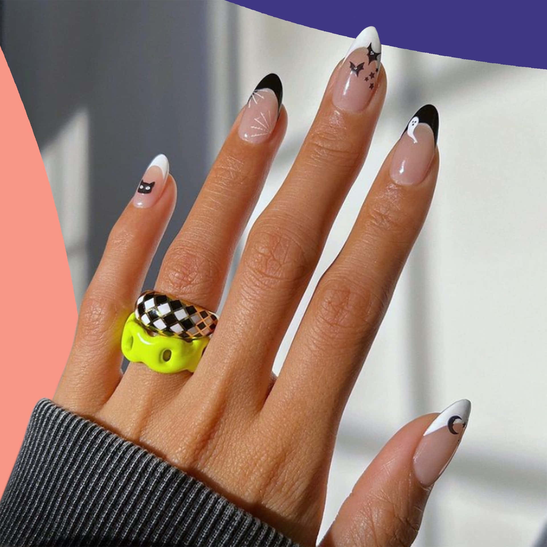 Halloween Nail Art 桌布 壁紙 — 一隻手帶有萬聖節主題指甲，飾有蝙蝠、鬼魂和貓咪，搭配大膽的霓虹戒指，背景為粉紅和紫色分割。