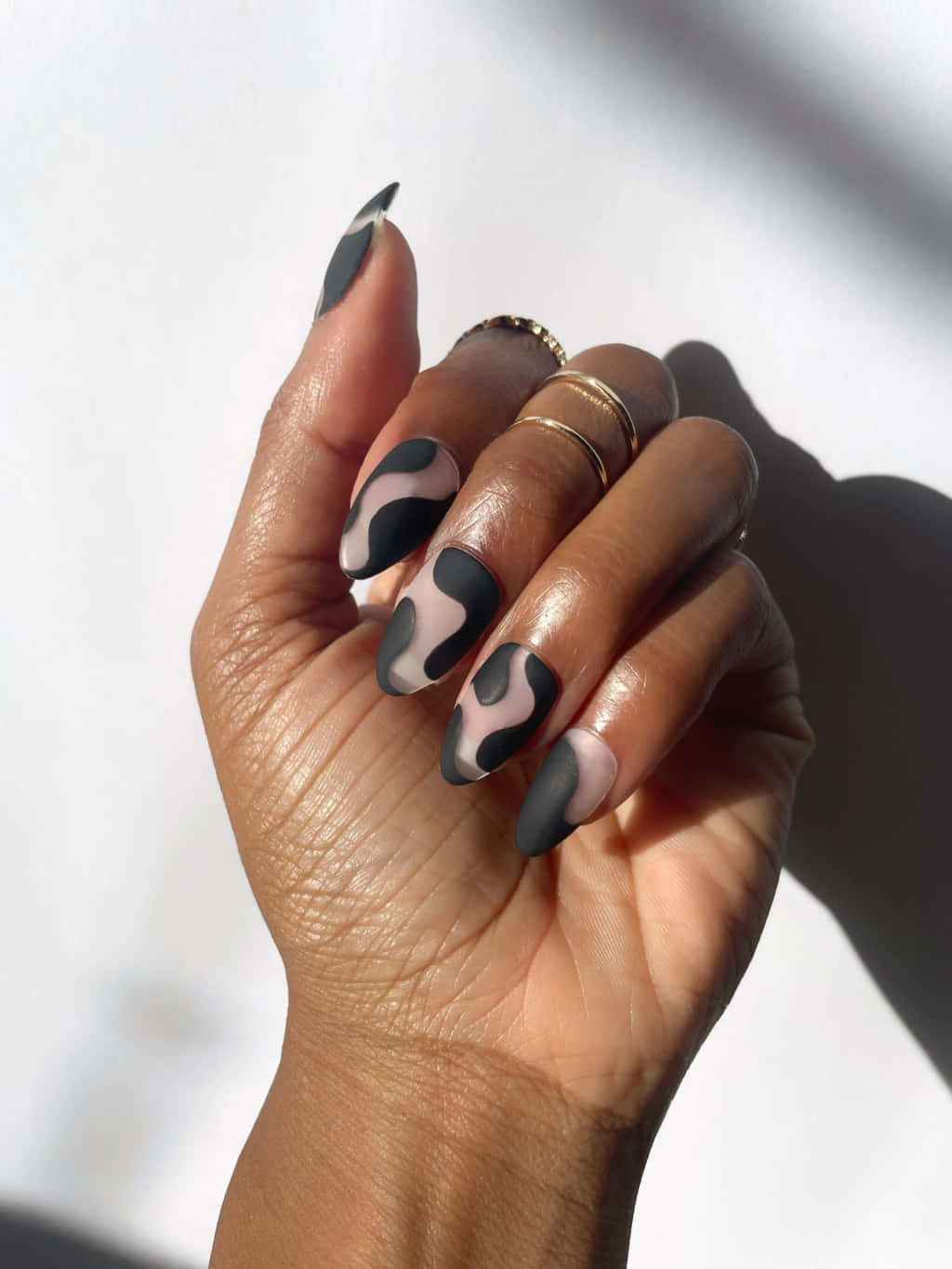 Nail Art 桌布 壁紙 — 一隻手帶有黑色和裸色乳牛紋指甲及金戒指，背景為明亮的白色，帶有強烈陰影。