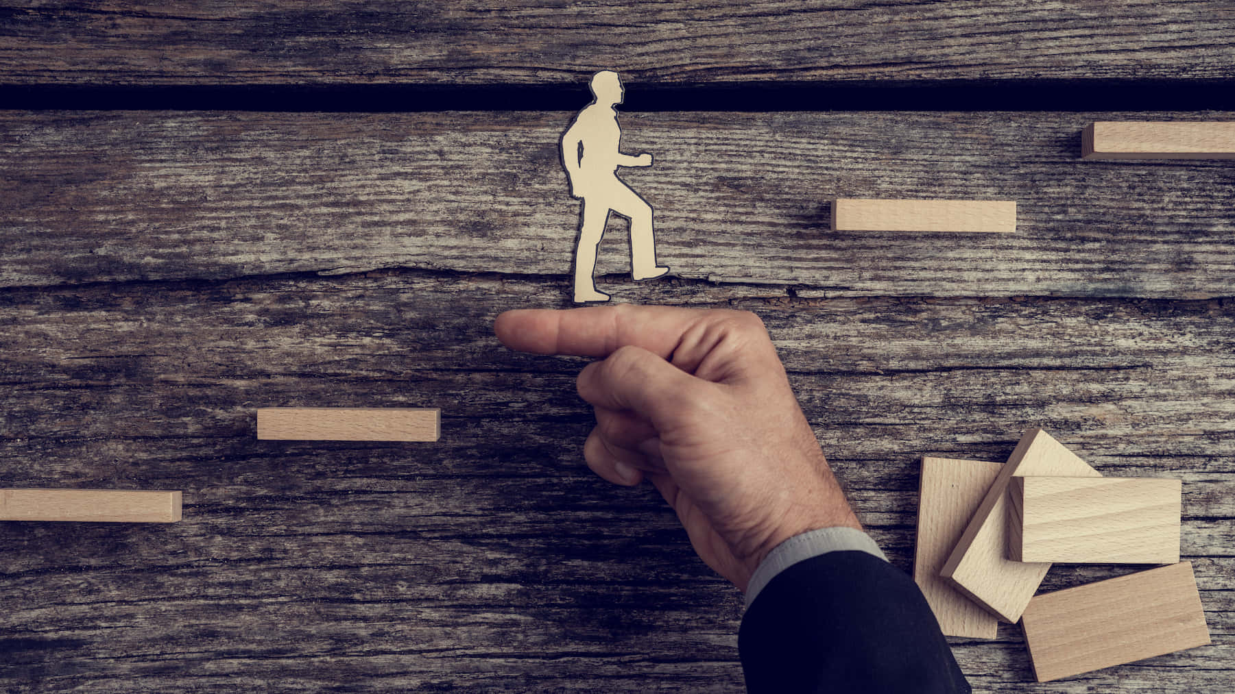 Leadership 桌布 壁紙 — 一隻手引導一個木製人物剪影穿過一個質樸的木質表面，上面散落著積木。