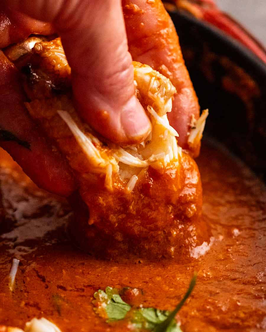 food iPhone 桌布 壁紙 — 一隻手從一個深色碗中濃郁的紅色醬汁裡拉出嫩滑的蟹肉，碗上點綴著新鮮的香菜。