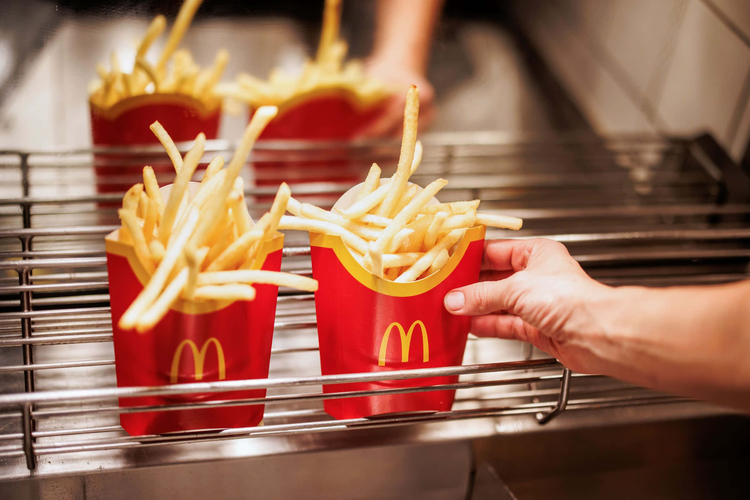 French Fries 桌布 壁紙 — 一隻手從廚房的金屬架上抓起一個裝滿金黃色薯條的紅色麥當勞薯條杯。