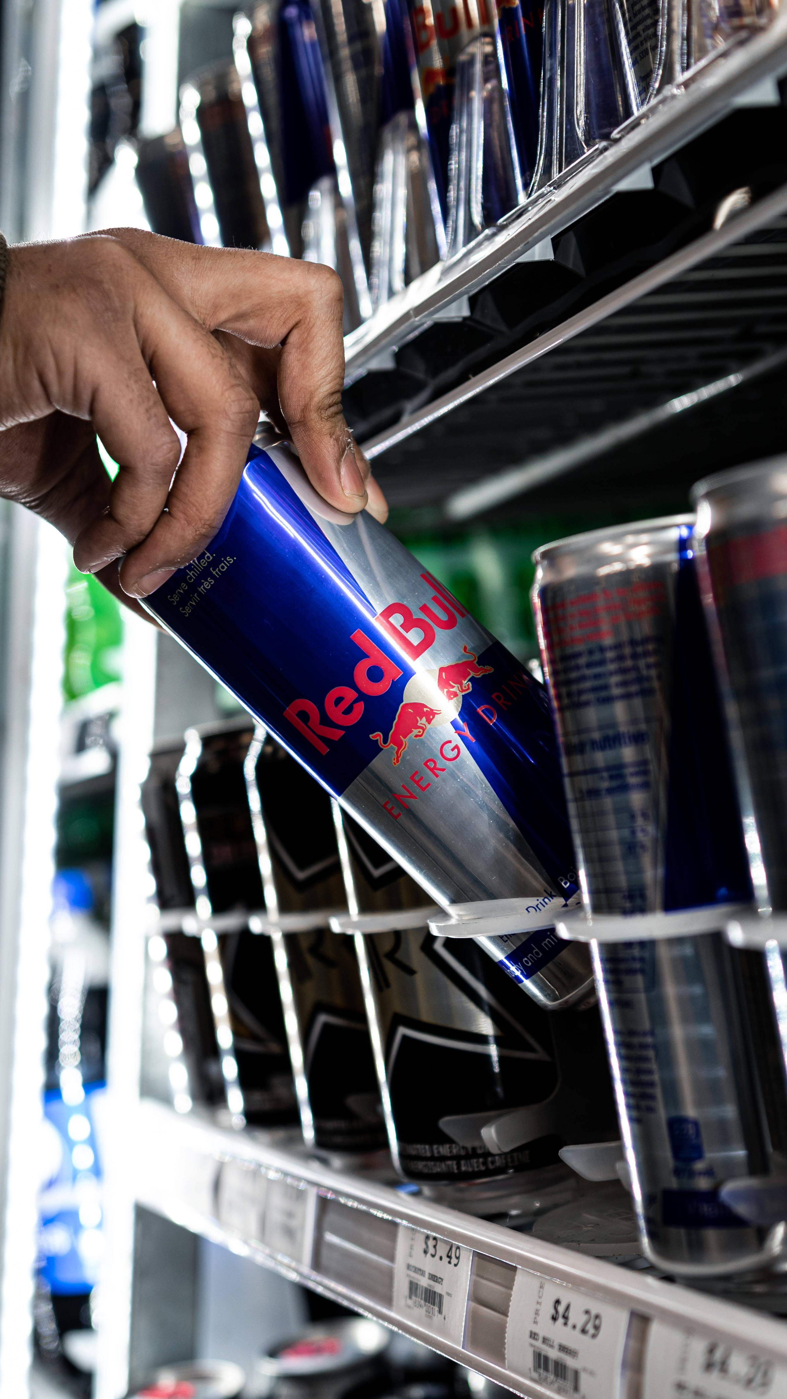 bull 桌布 壁紙 — 一隻手從明亮照明的冷藏貨架上抓起一罐Red Bull，貨架上擺滿了能量飲料。